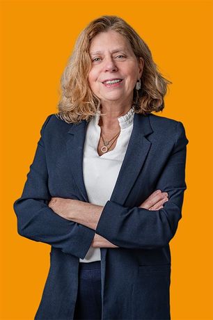 Een vrouw in een blauw pak en een wit overhemd staat met haar armen over elkaar.
