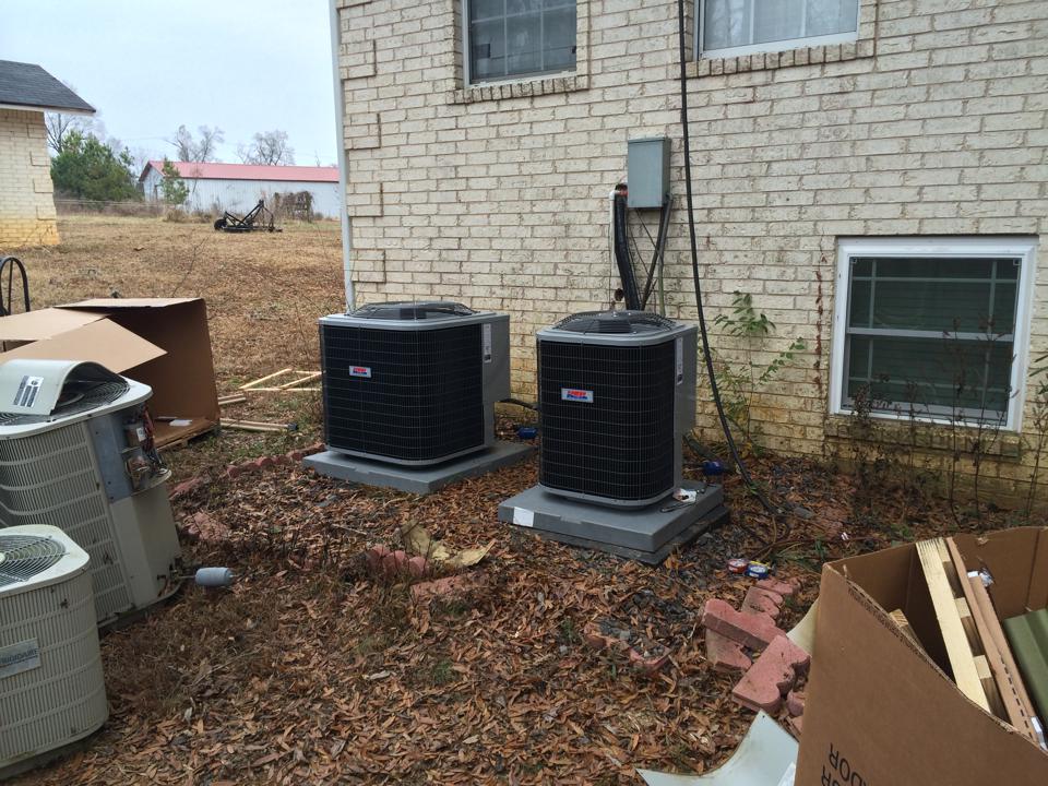 Two air conditioners are sitting outside of a brick house