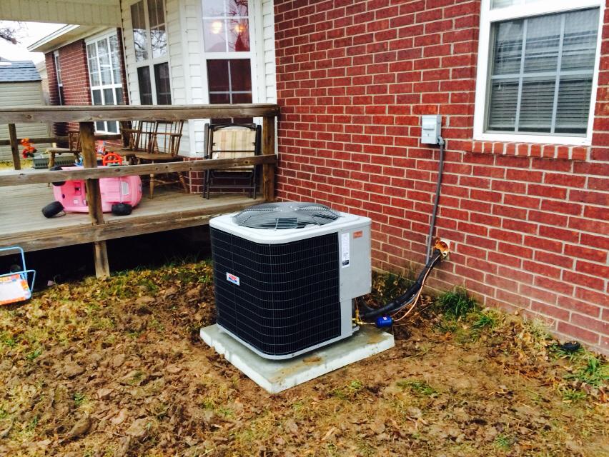 An air conditioner is sitting on the side of a brick house.