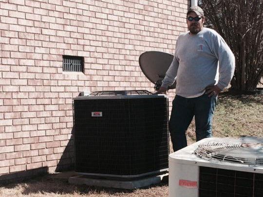 A man is standing next to an air conditioner outside of a brick building.