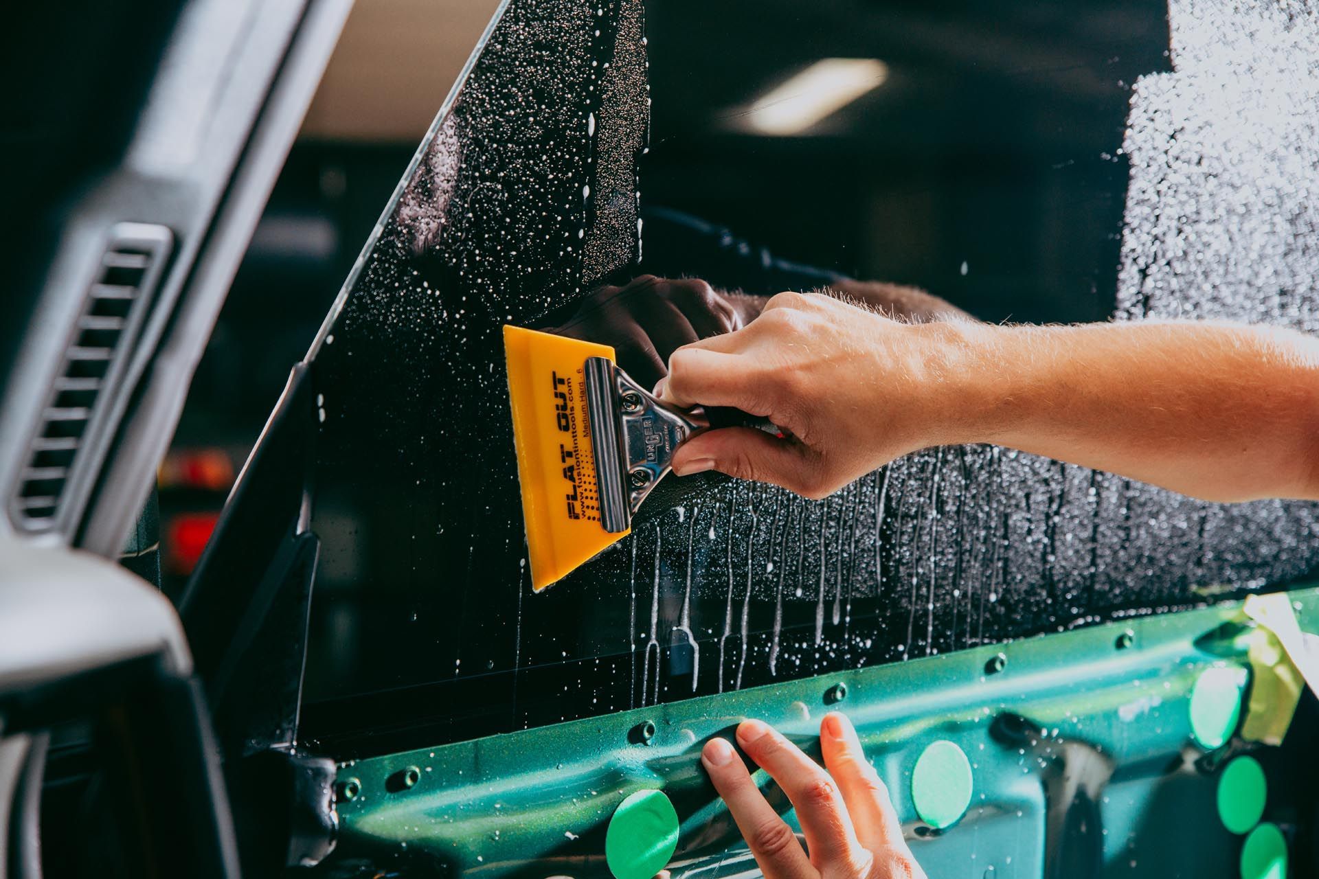 Hand using a squeegee to clean a green car window