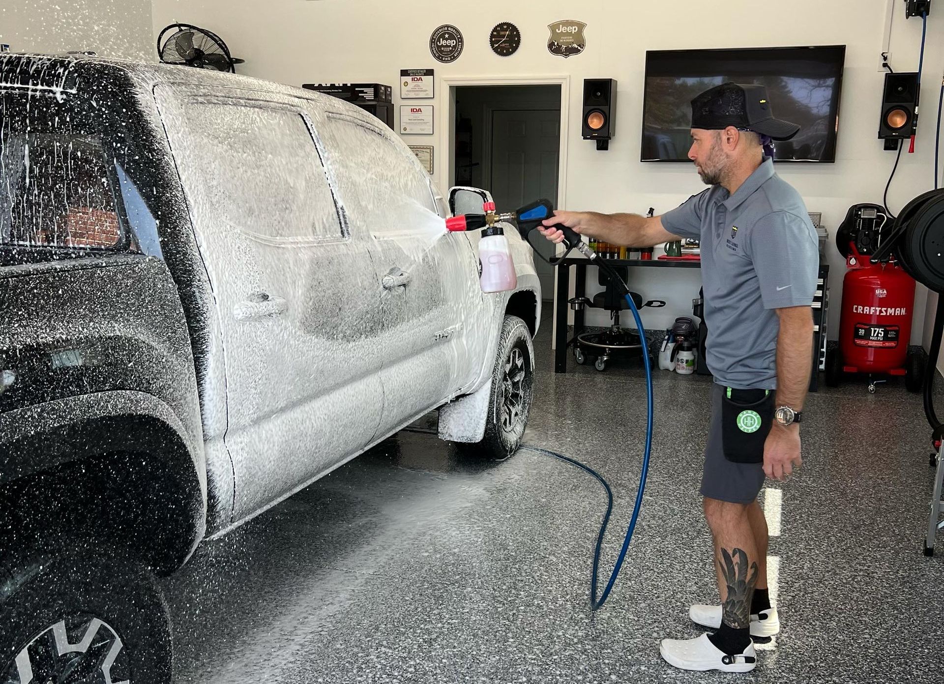 A man is washing a truck with foam in a garage.