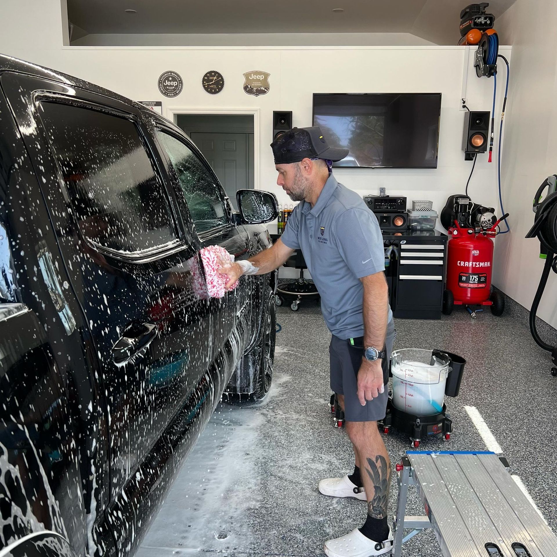 A man is washing a black truck in a garage.