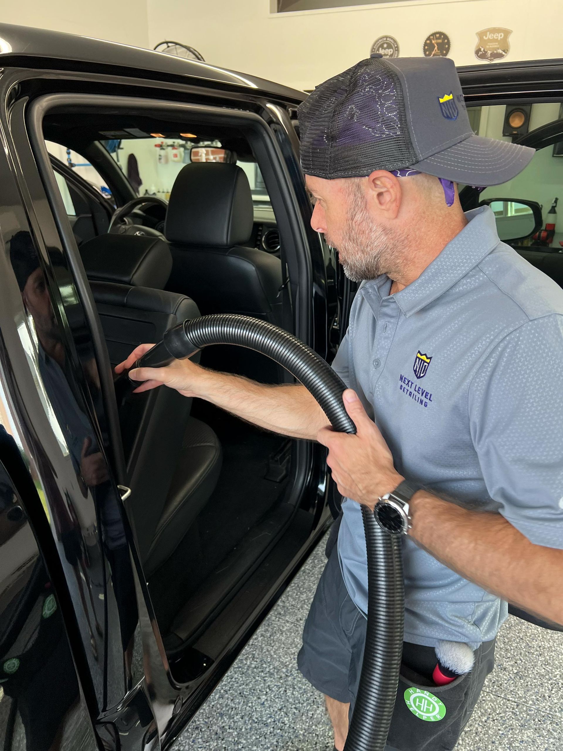 A man is using a vacuum cleaner to clean the inside of a car.