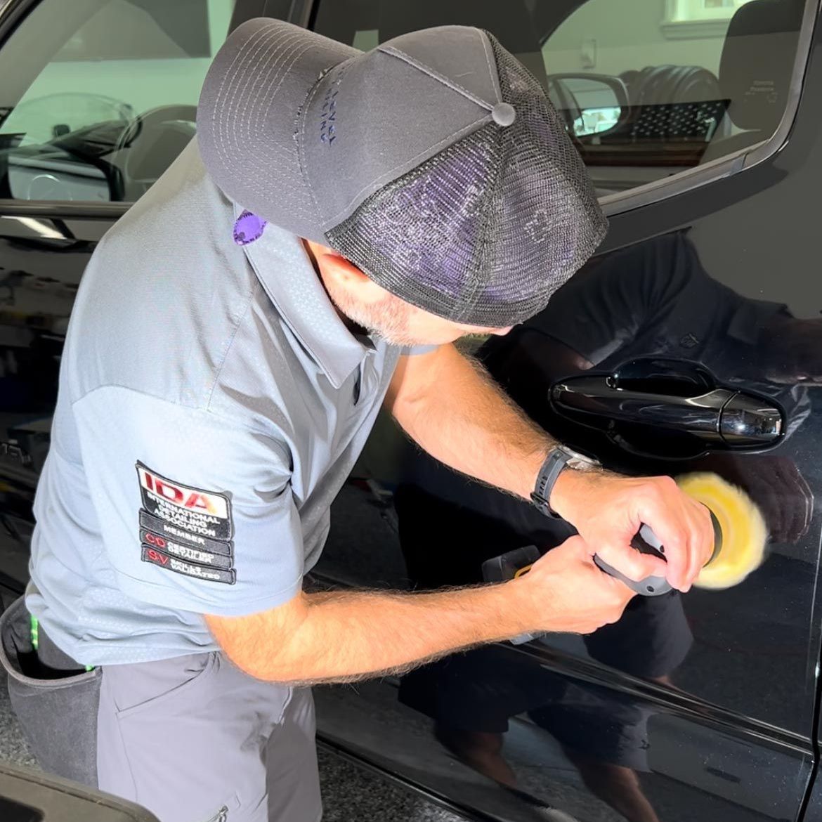 A man wearing a hat is polishing a car