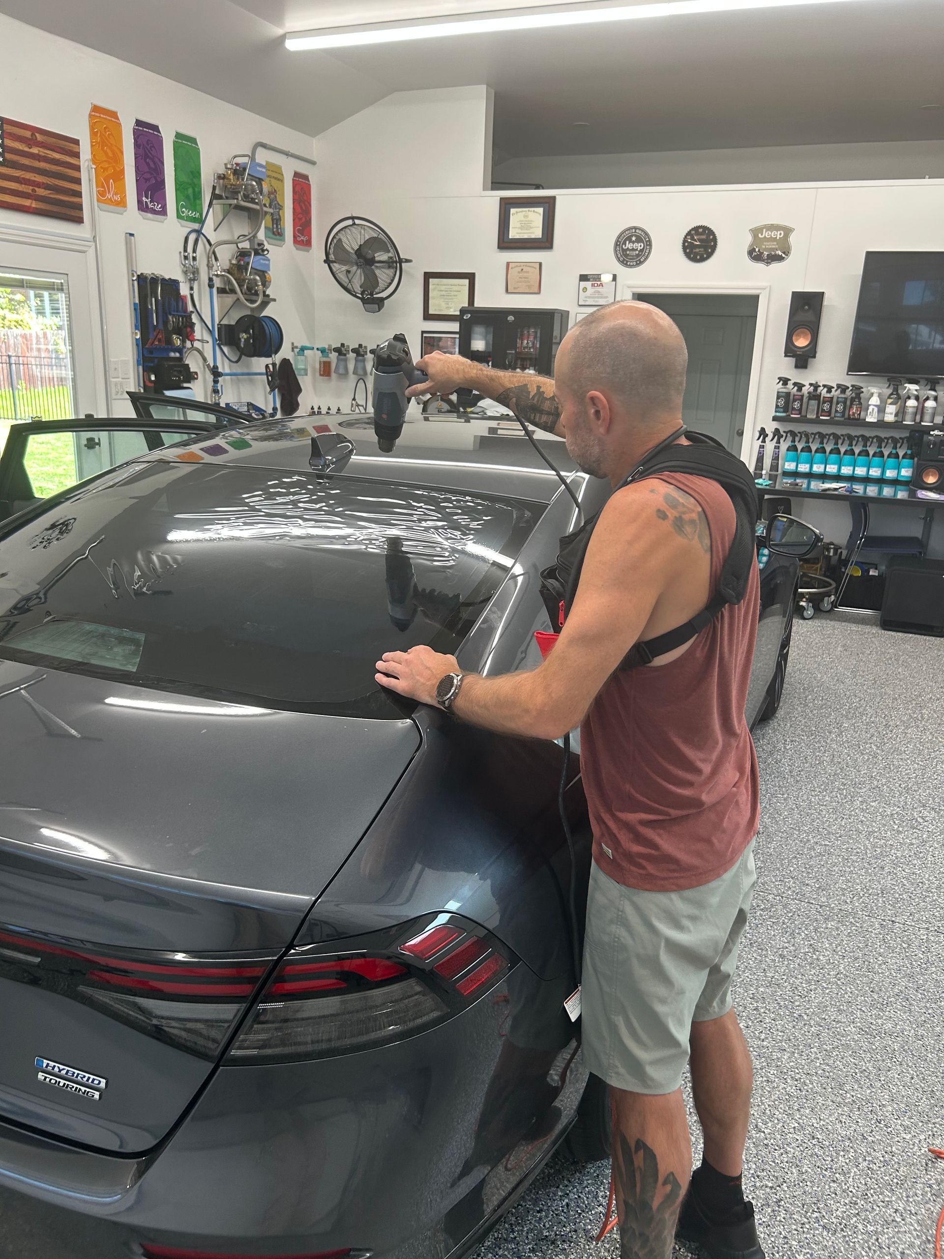 Man in a garage applying wrap film to a gray sedan roof and rear window