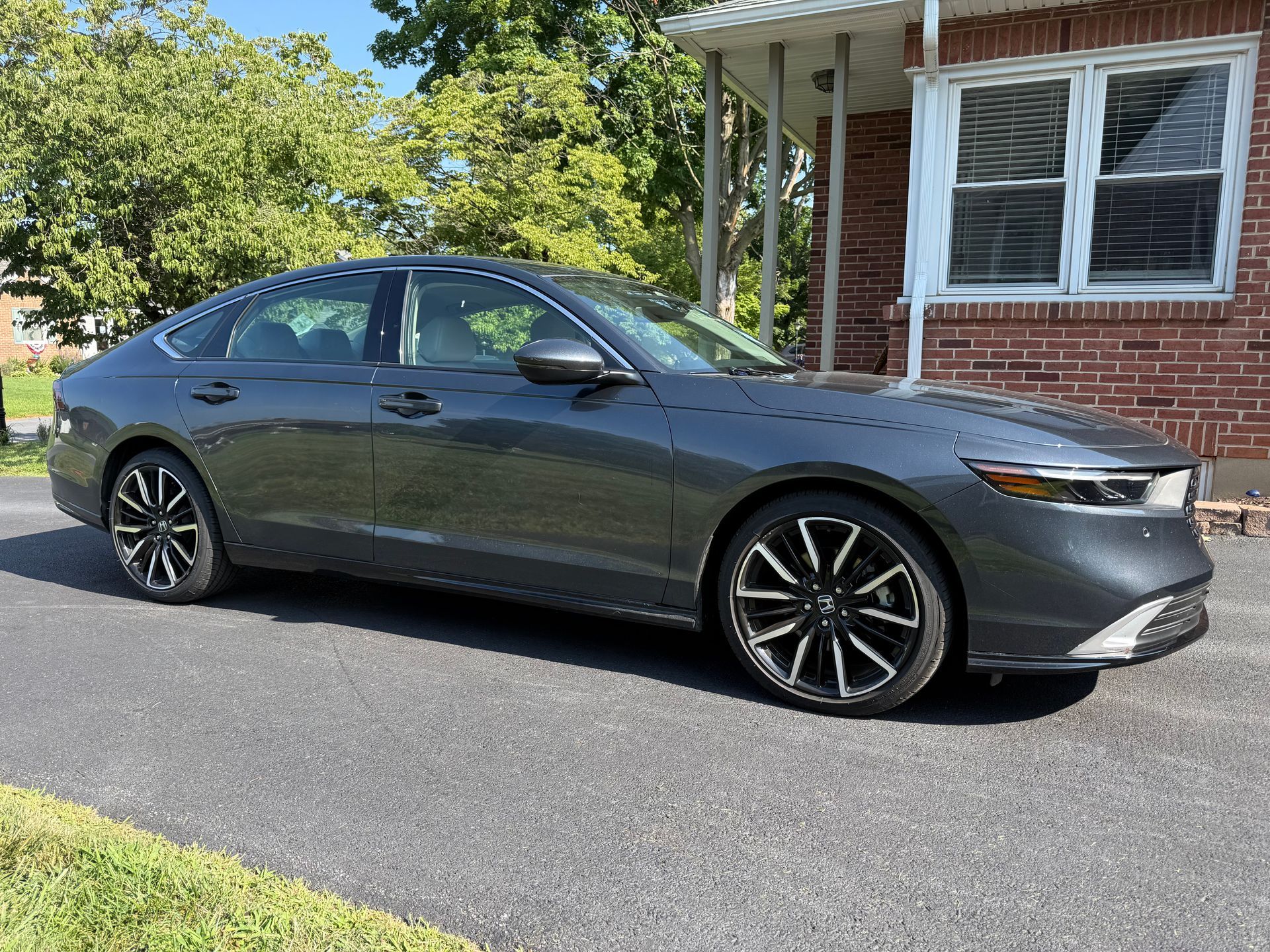 Gray sedan parked in a driveway beside a brick house