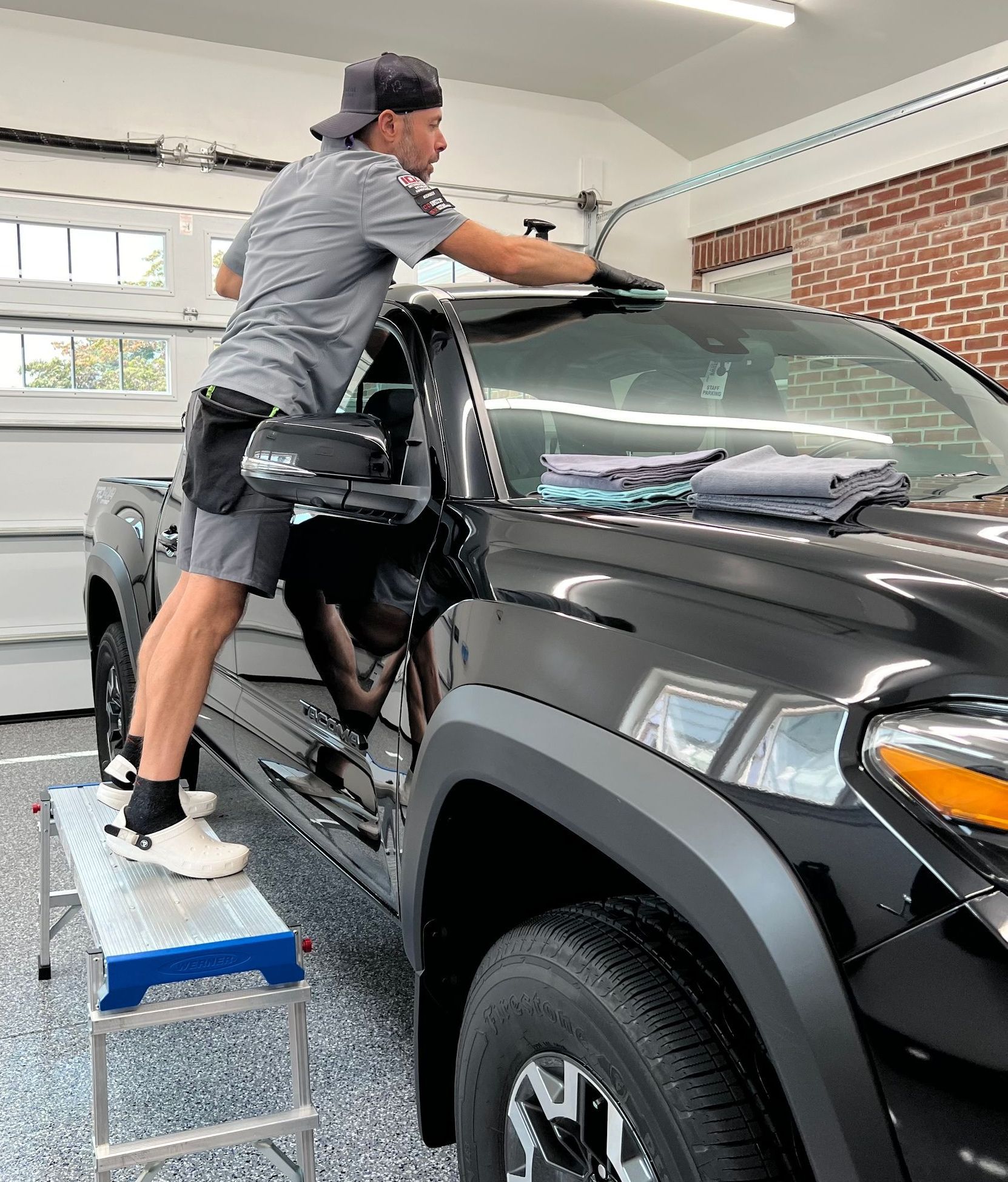 A man is cleaning the windshield of a black truck in a garage.