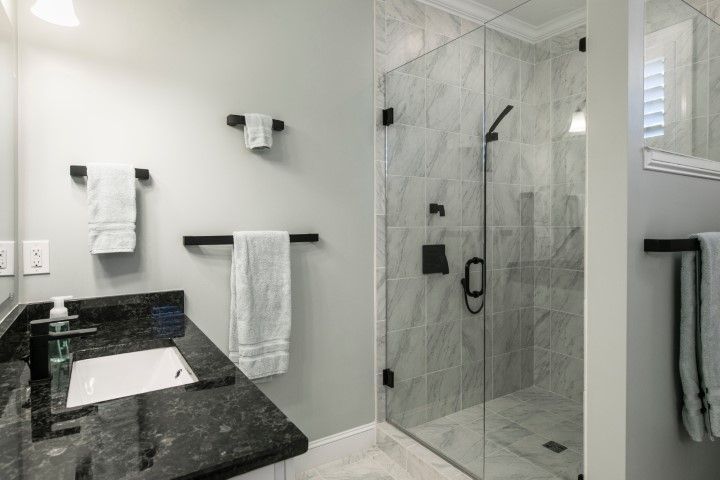 Modern bathroom with black vanity, white sink, glass shower, and tiled walls