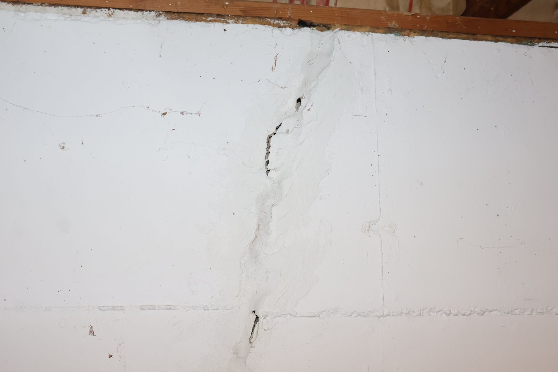A vertical crack runs through white painted concrete blocks under a wooden beam.