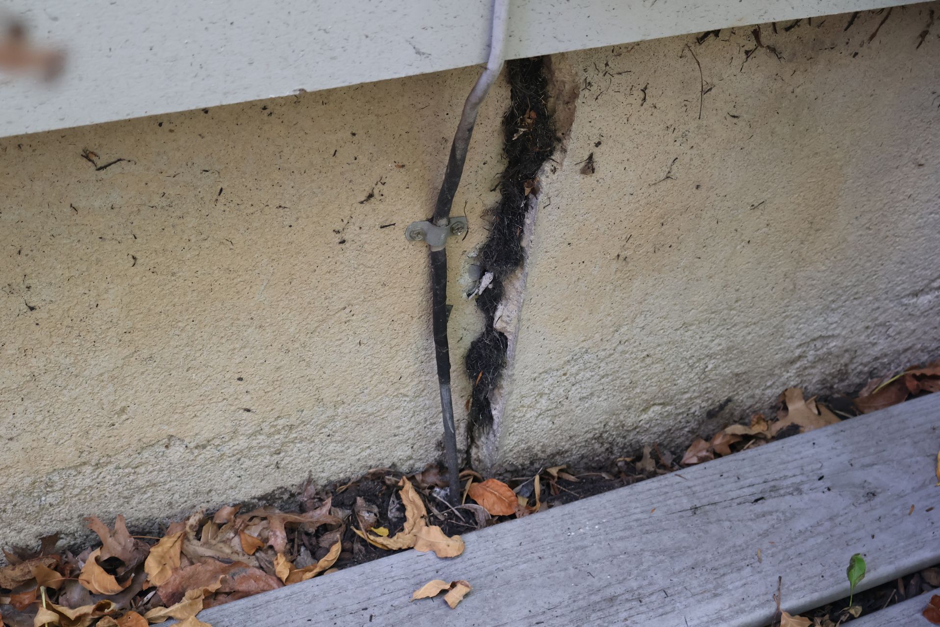 A vertical crack in a tan stucco foundation wall with an electrical conduit pipe running beside it.