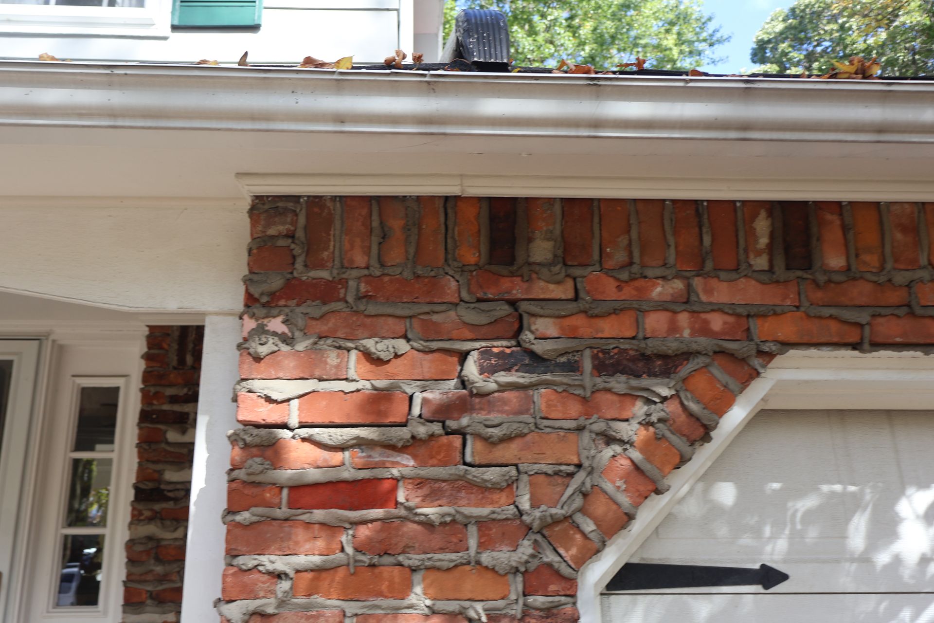 A brick wall above a garage door shows signs of structural settling with a prominent vertical crack through the mortar.
