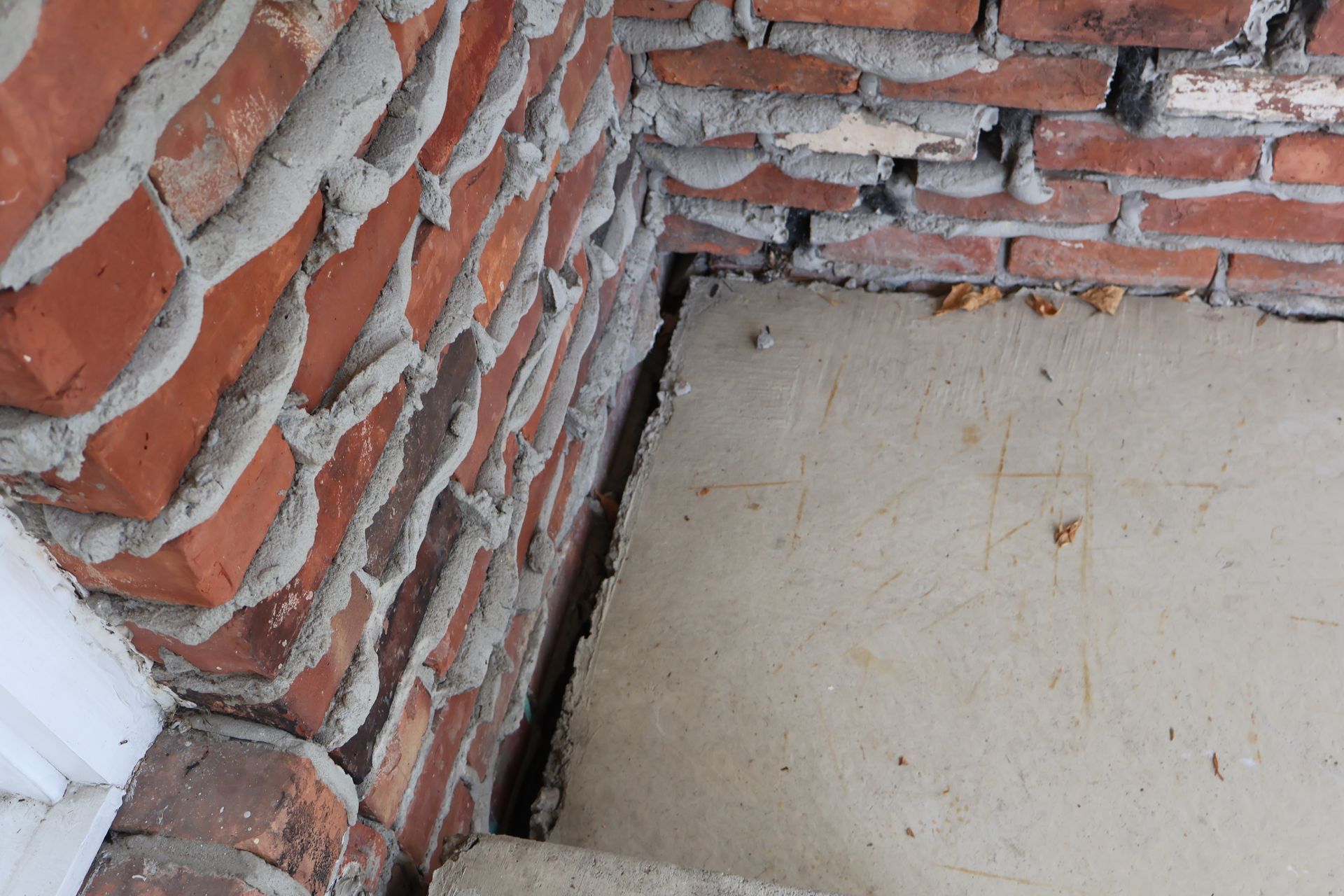 A corner junction where a rough, unfinished brick wall meets a light-colored concrete slab, showing a visible gap.