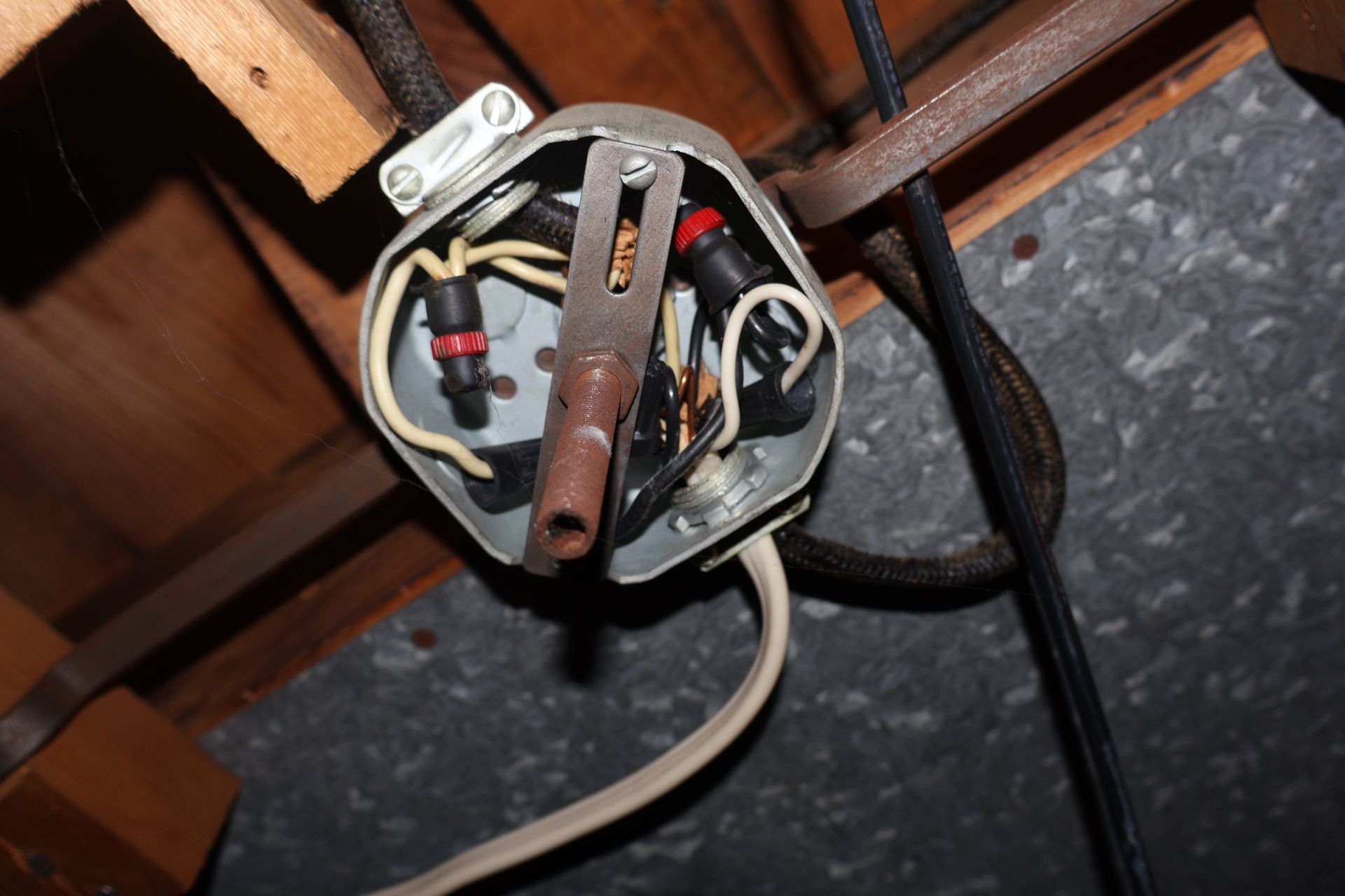 Open metal electrical junction box mounted on wood beams with wires connected by black caps and a central metal bracket.