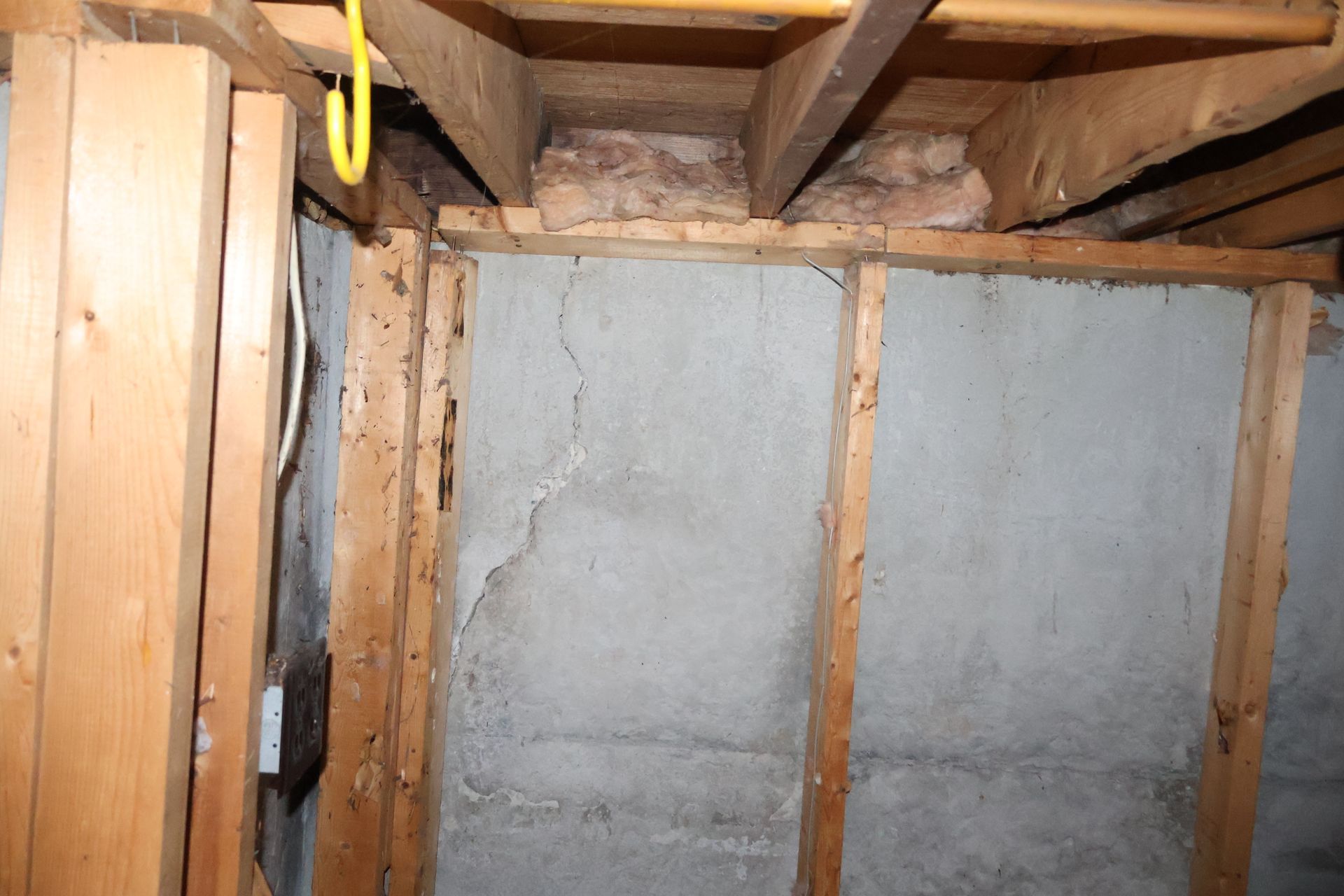 A concrete basement wall featuring a diagonal structural crack, framed by wooden studs and exposed floor joists above.