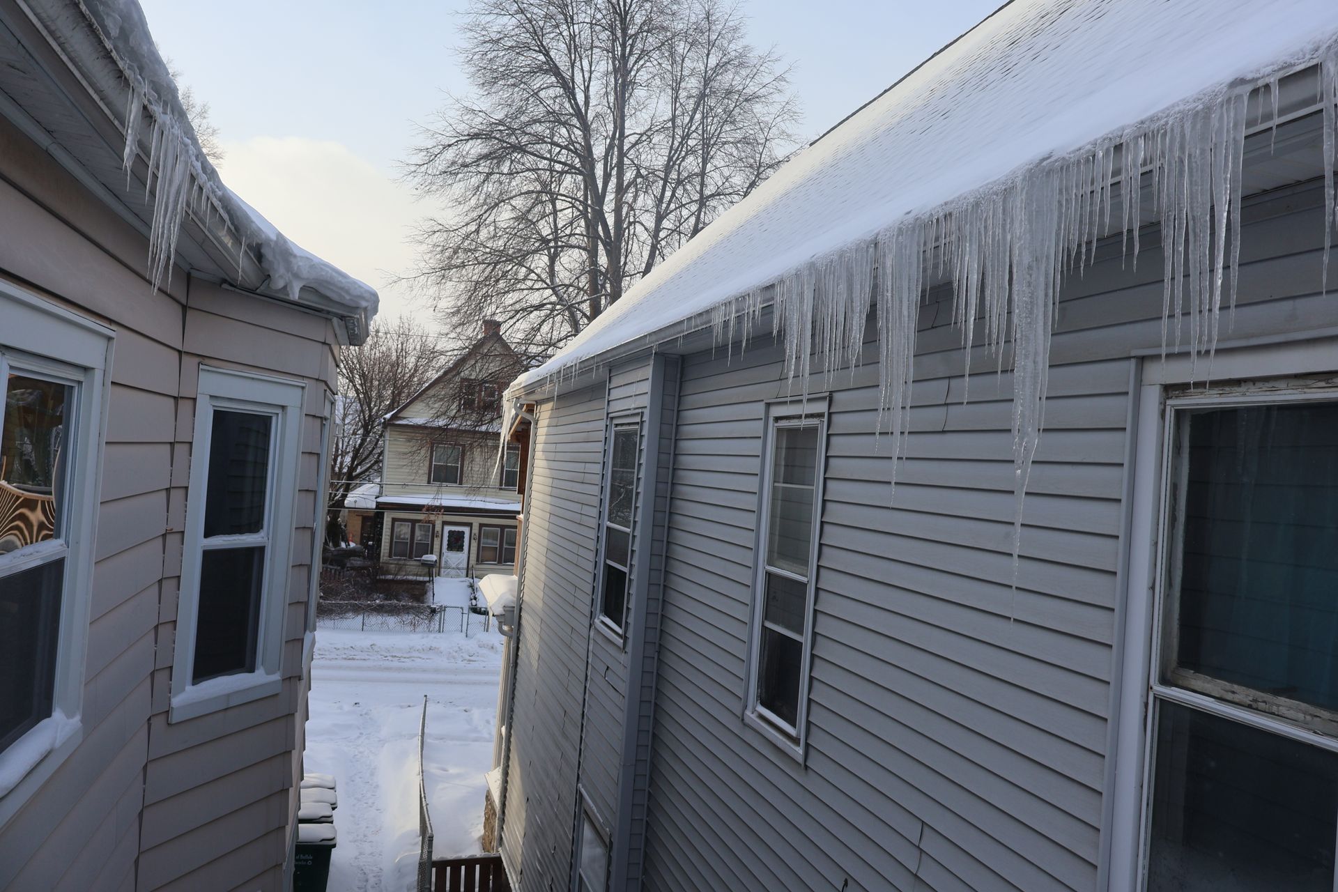 View from between two houses showing a snowy street with icicles hanging from the roof eaves.