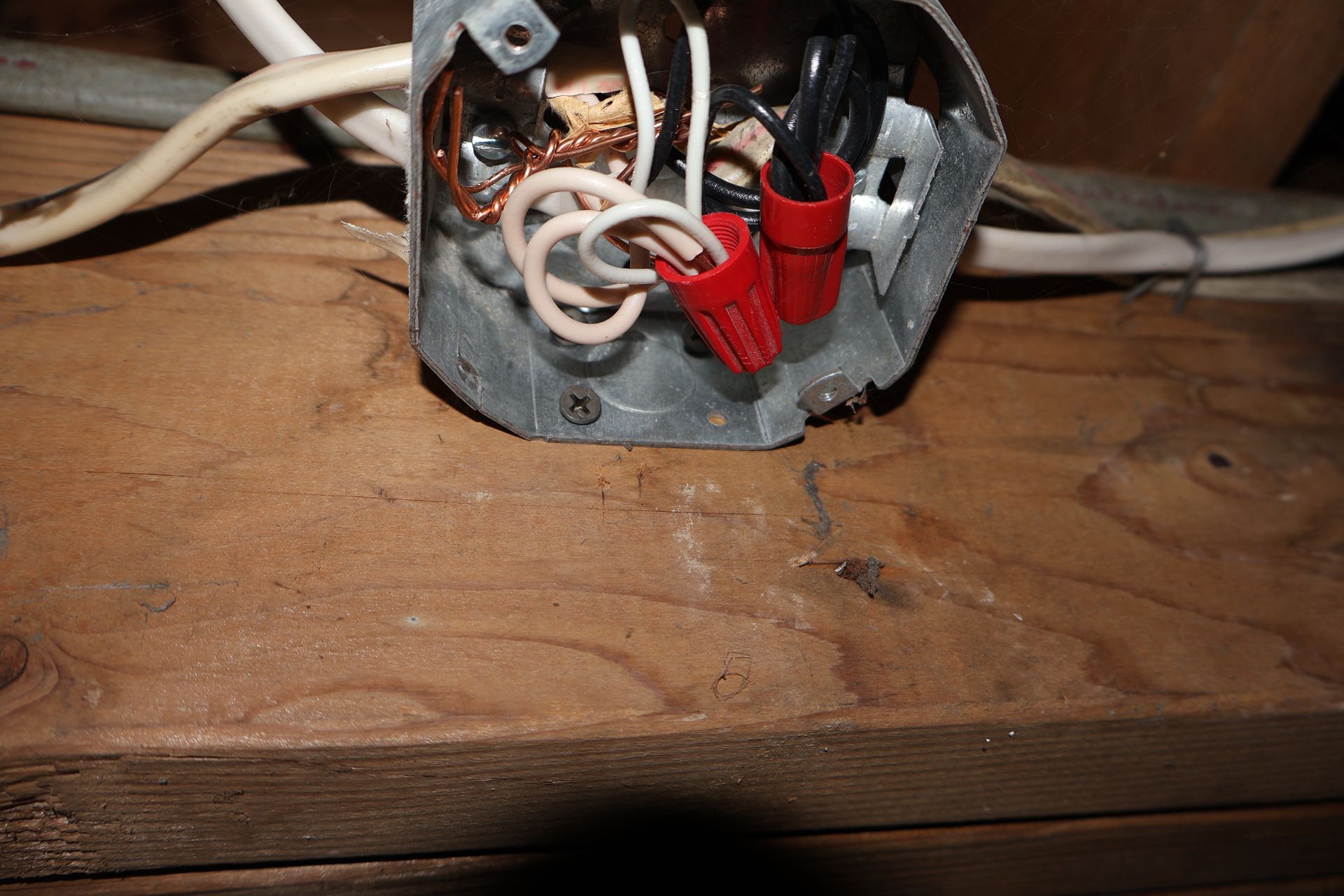 An electrical junction box mounted on a wooden beam contains wires connected with red wire nuts.