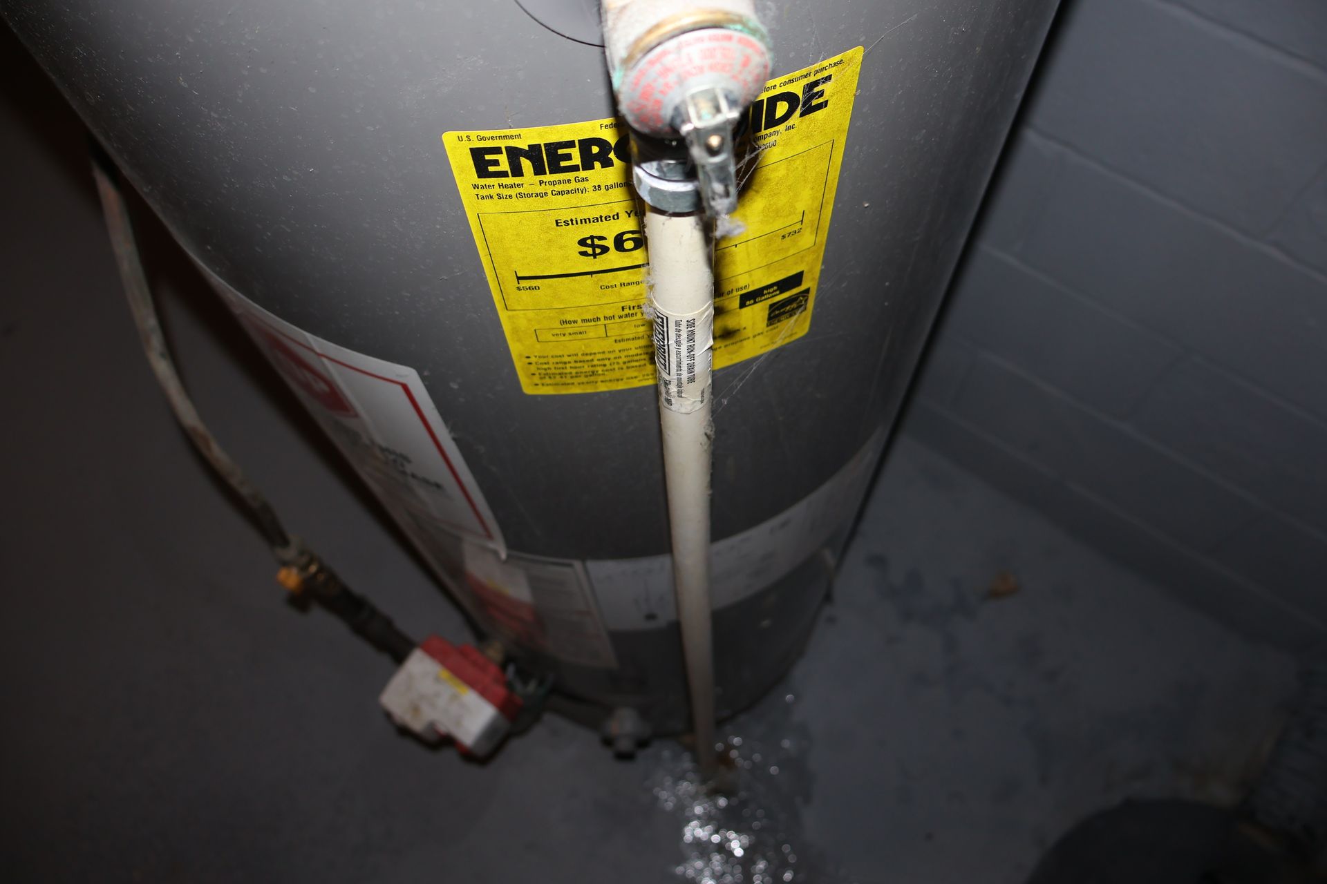 A water heater with a temperature and pressure relief valve discharge pipe leaking onto the concrete floor.