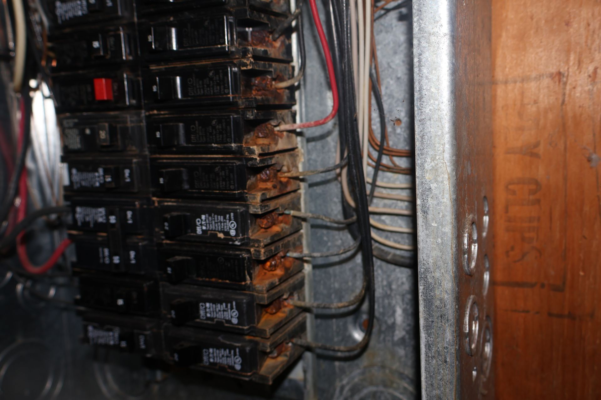 An open electrical panel featuring a column of black circuit breakers with exposed wiring and visible rust buildup.