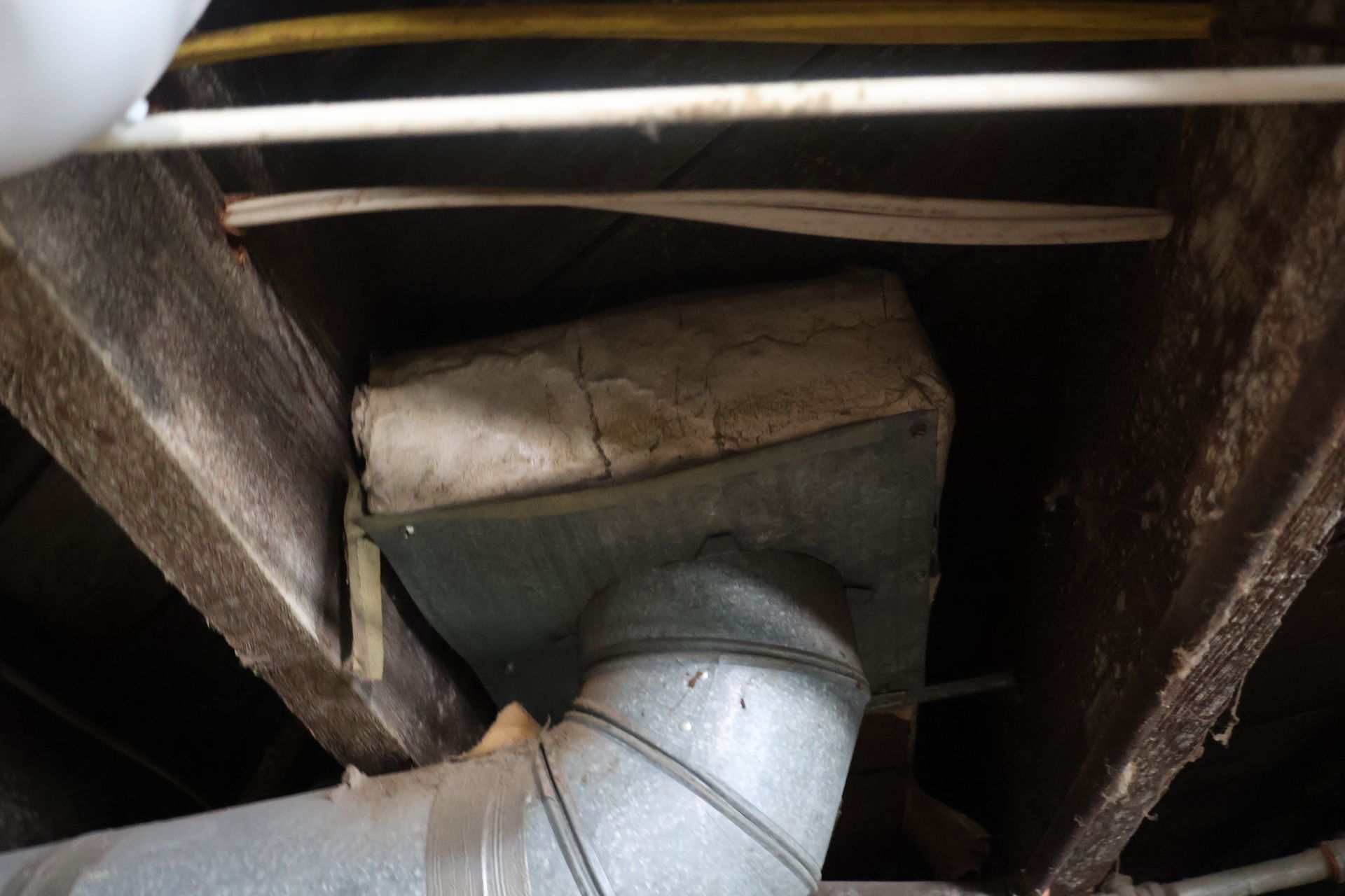 Metal HVAC ductwork with insulation installed between wooden floor joists in an unfinished basement.