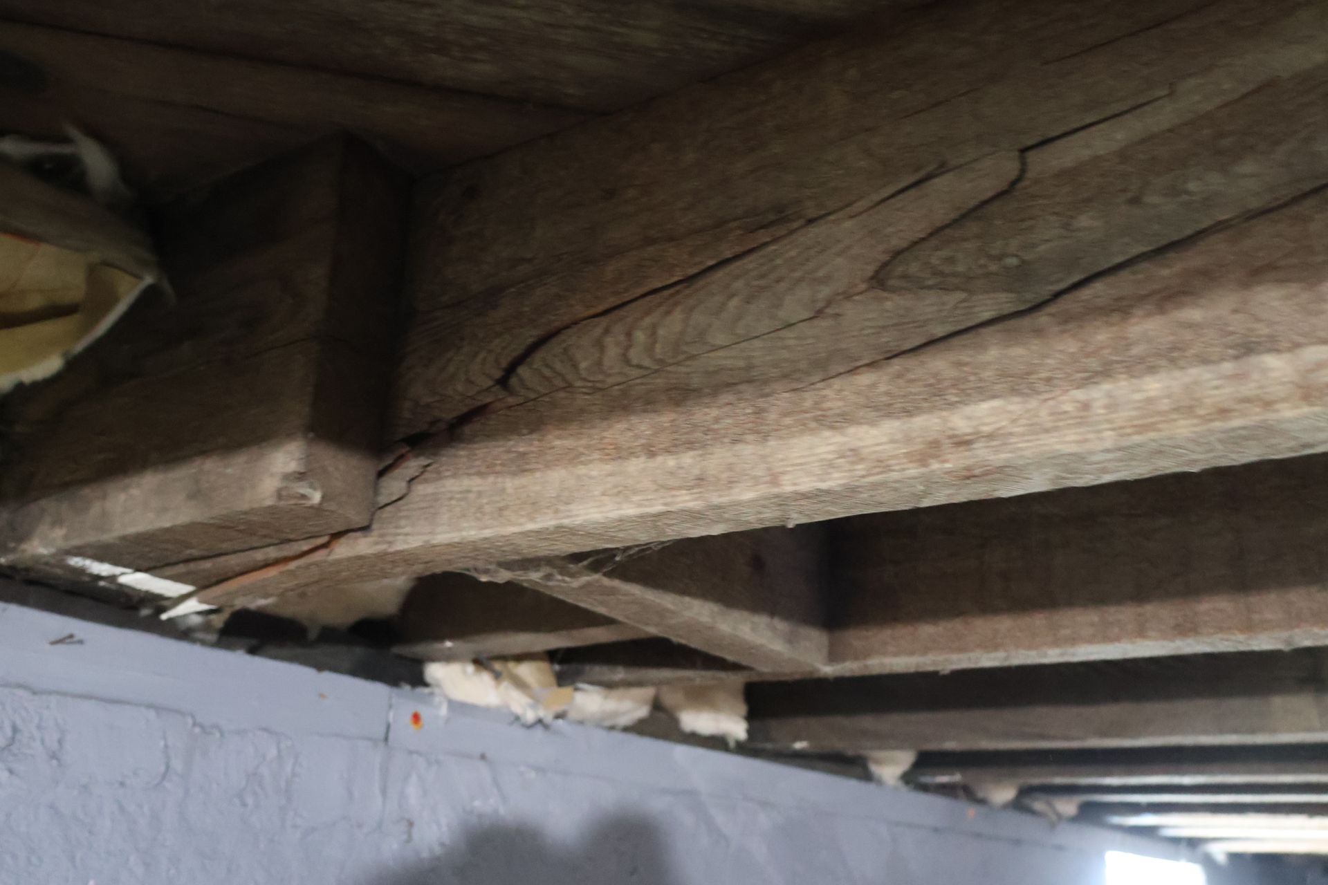 A wooden floor joist with a prominent diagonal crack near where it connects to the foundation wall.