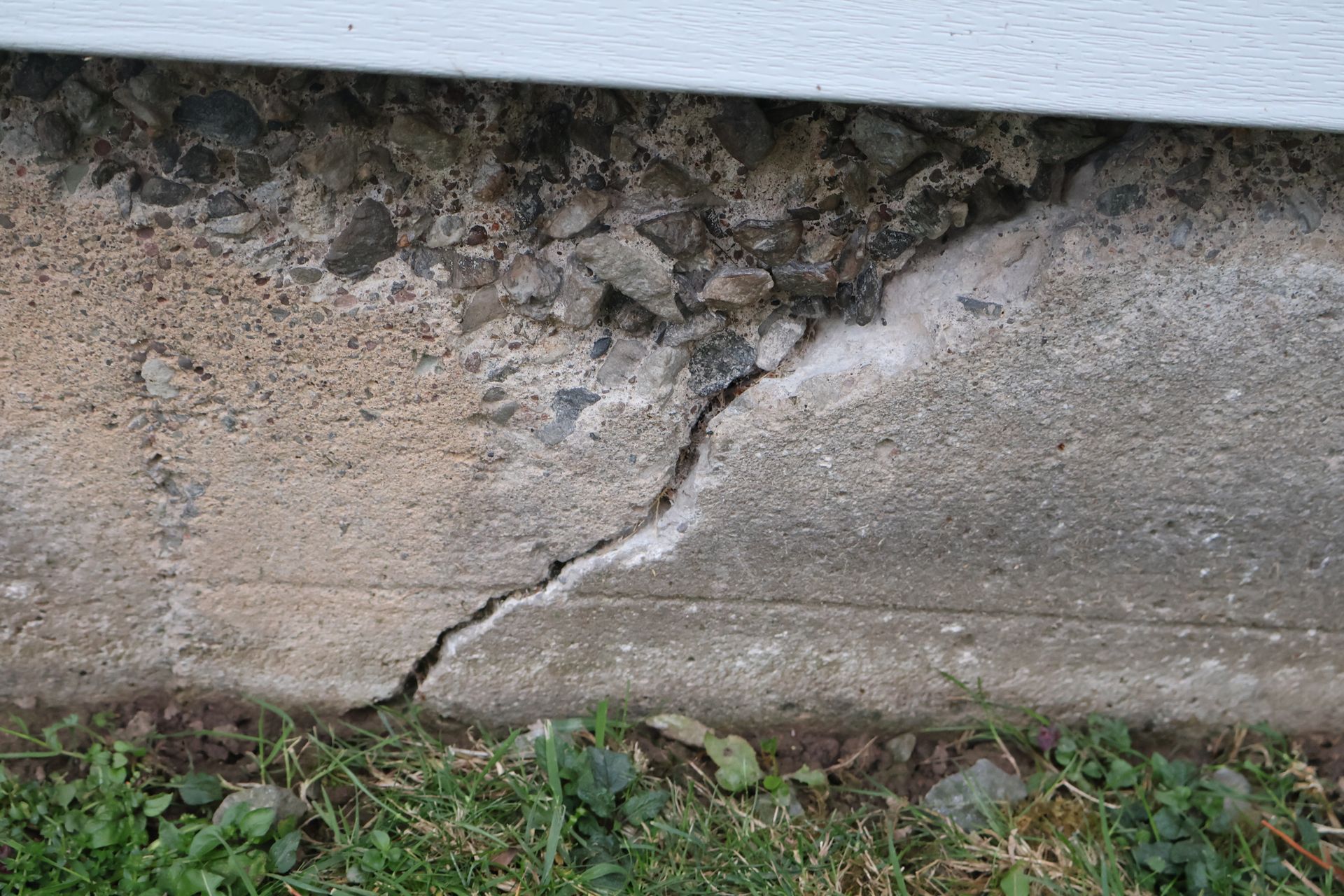 A diagonal crack running through a gray concrete house foundation, showing exposed aggregate near the top.