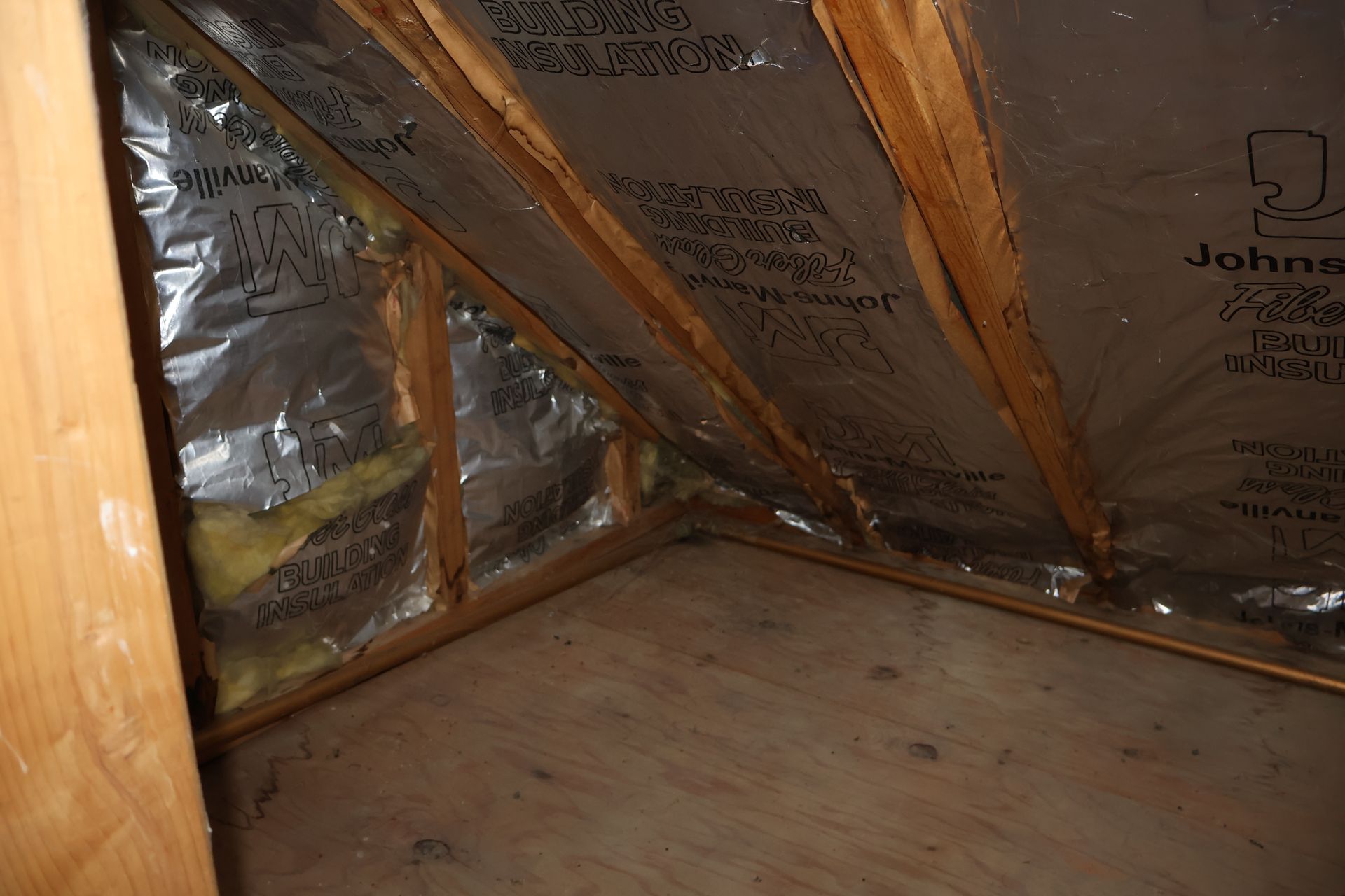 An attic crawl space featuring exposed wooden rafters and fiberglass insulation with a silver, reflective foil backing.