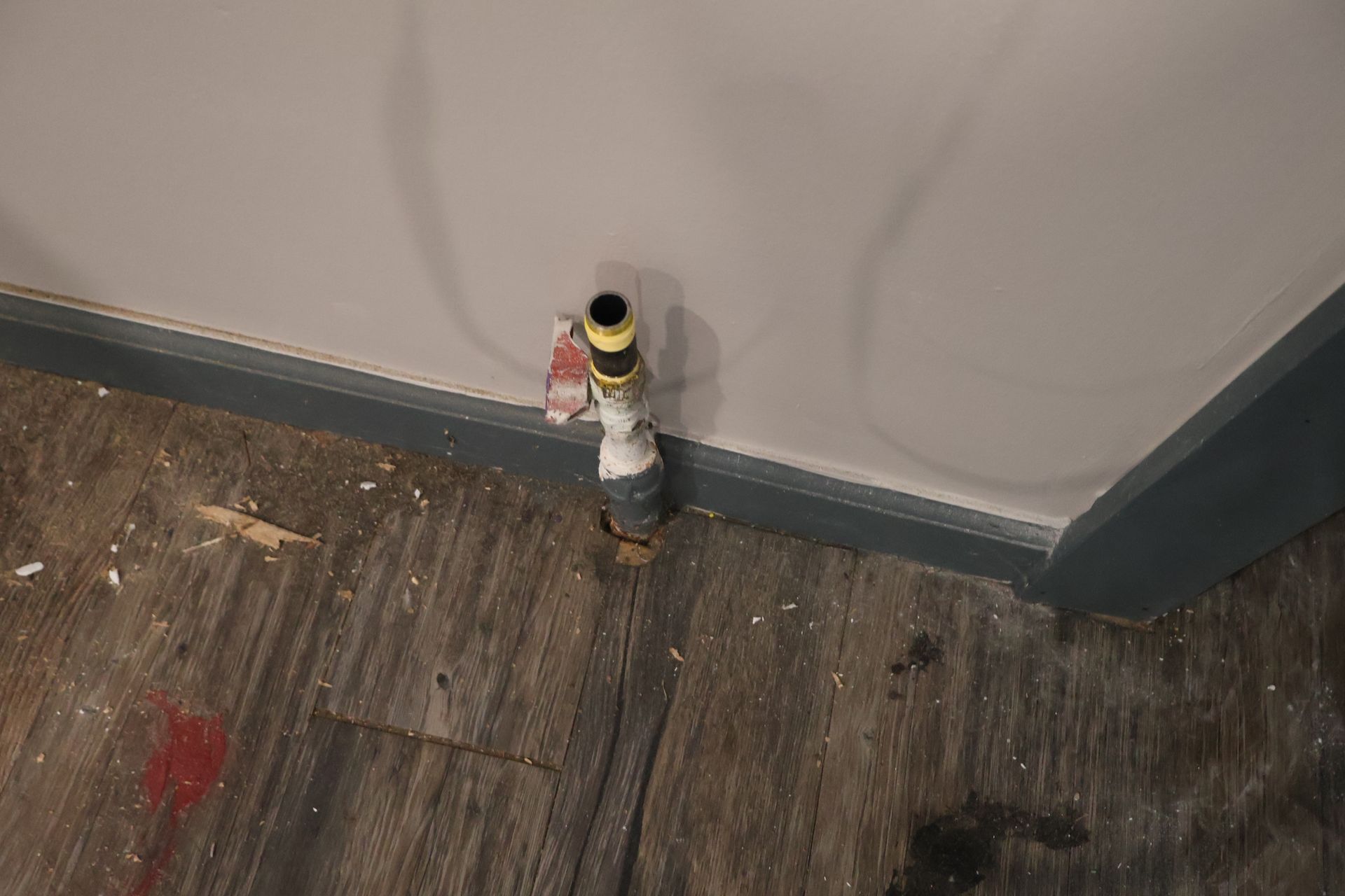 A gas valve pipe sticking out of the floor against a wall with a grey baseboard in a room under construction.