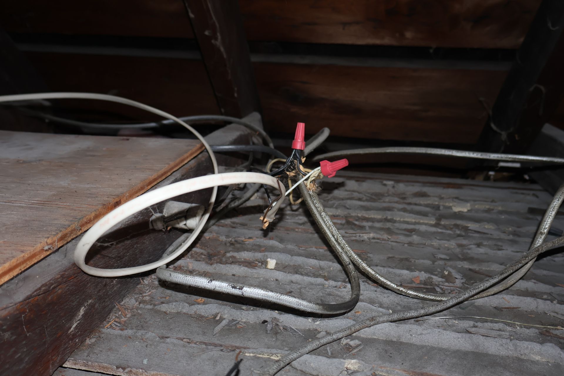 Exposed electrical wiring with red wire nuts and bare copper connections lying on an attic floor.