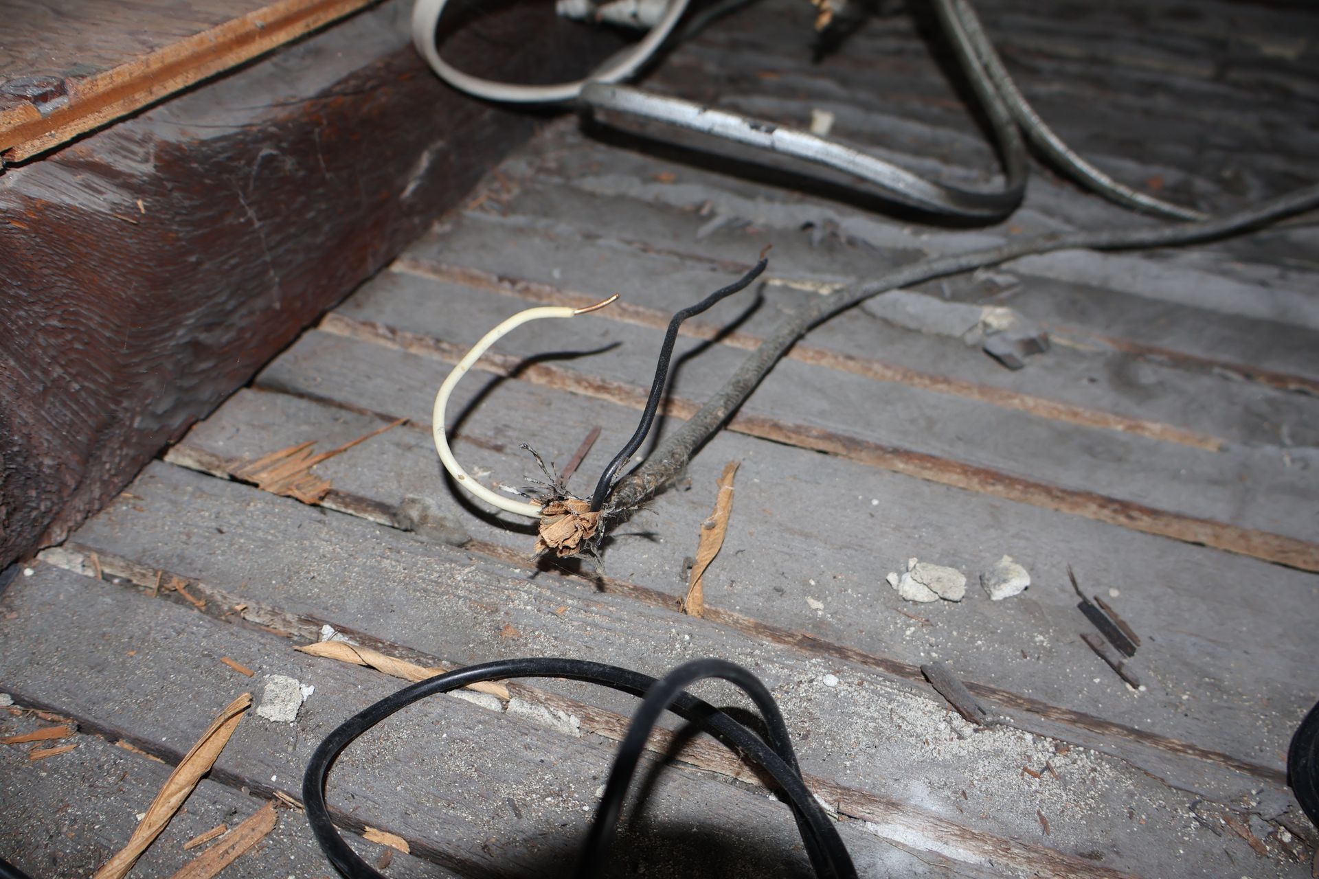 Exposed electrical wires and a junction knot resting on wooden floorboards in an attic space.