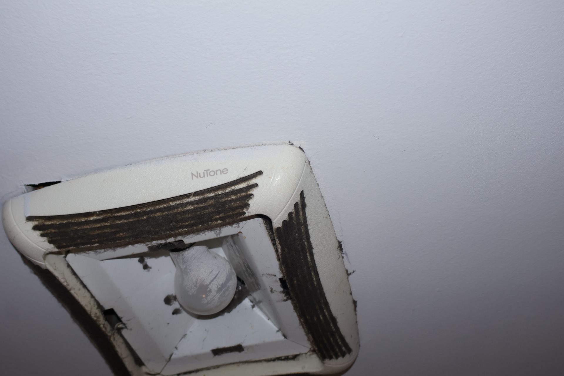 A dirty NuTone ceiling fan and light fixture with thick, dark dust buildup on the intake vents.