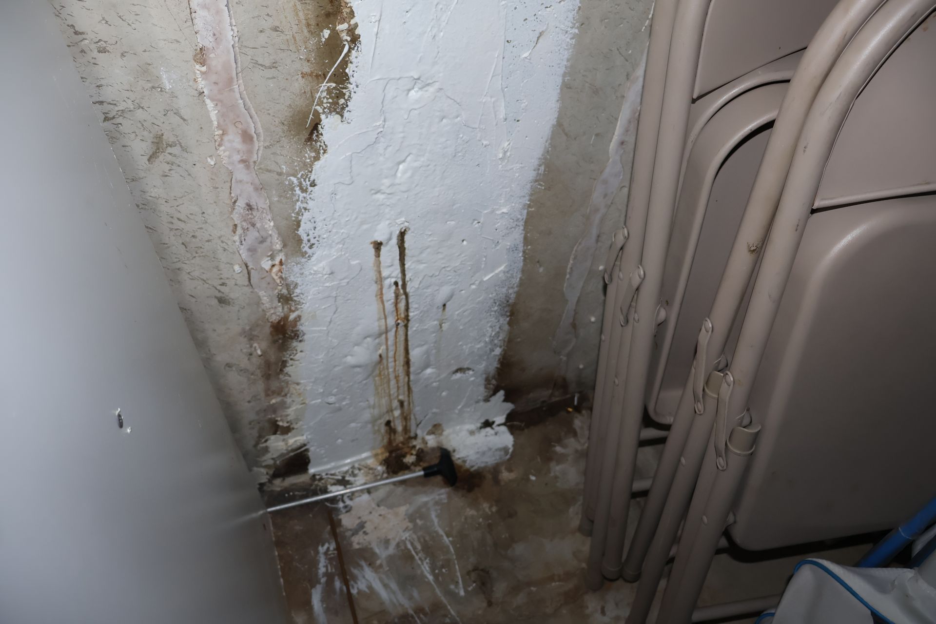 A white, patched concrete basement wall showing signs of water damage, rust streaks, and moisture at the floor junction.