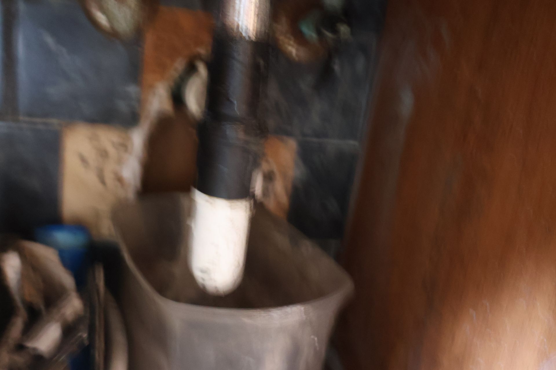 A blurry close-up of a pipe with a white end dripping into a plastic container under a sink.