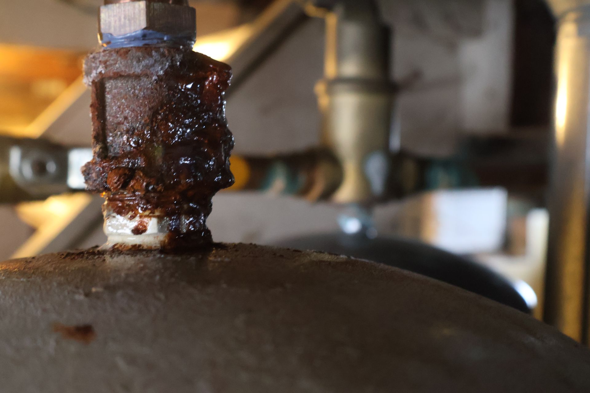 A close-up view of a rusted metal pipe fitting attached to a tank, showing signs of corrosion and potential leakage.