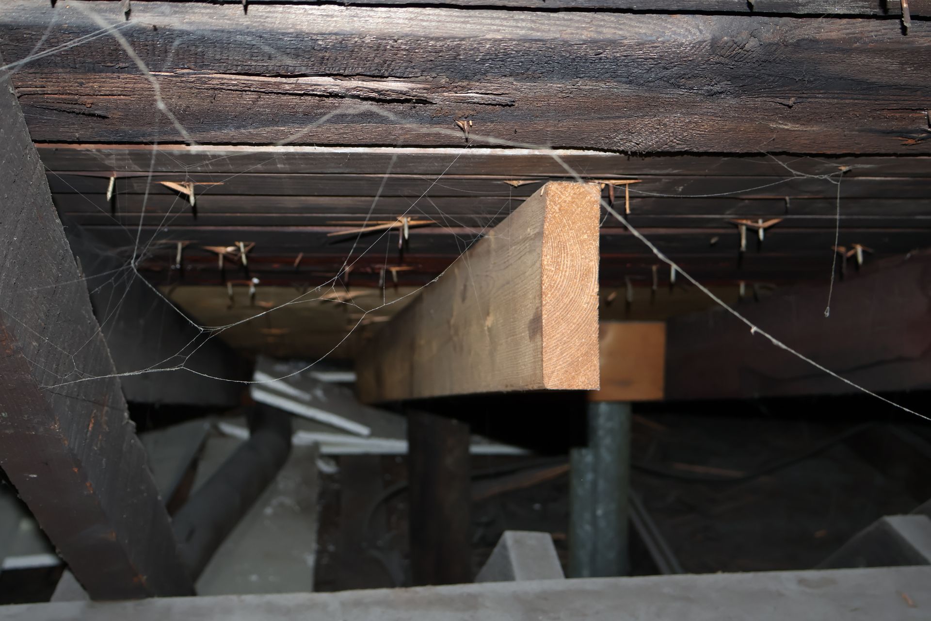 Looking up into an attic space at exposed wooden joists, dark weathered roof decking, and a new support beam.