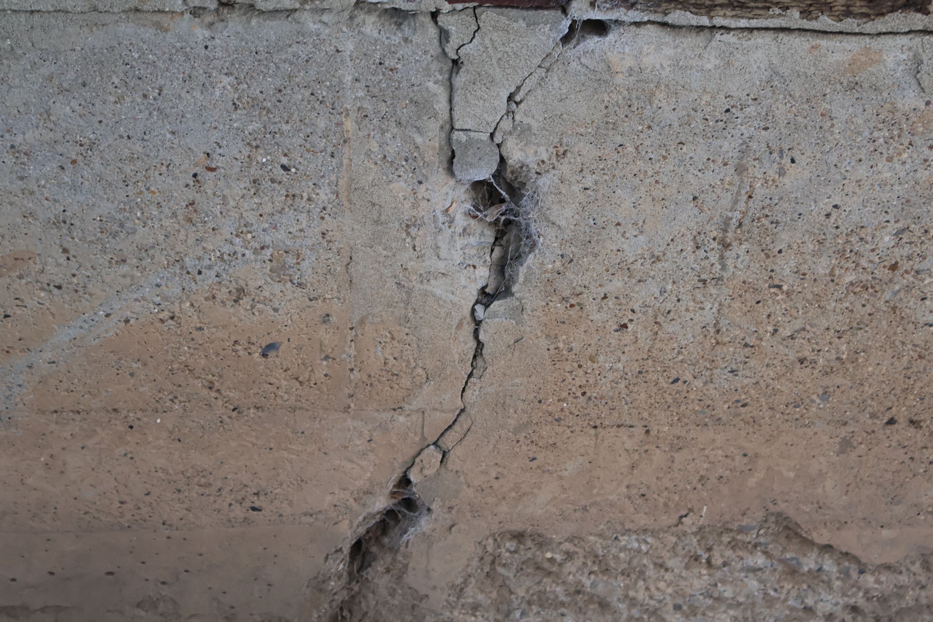 A vertical crack in a rough, textured concrete surface with some loose debris inside the fissure.