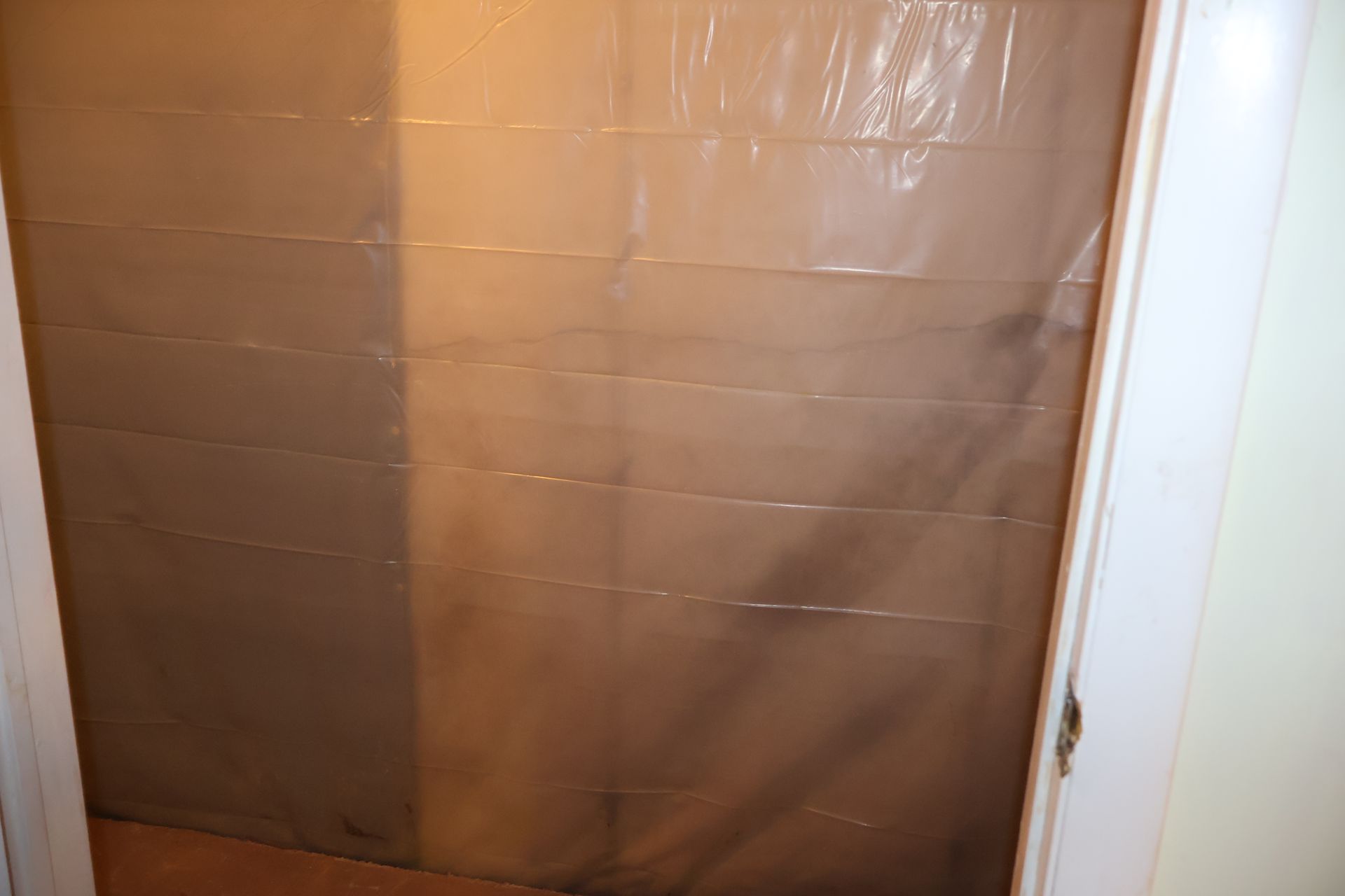 A doorway covered with thin, clear plastic sheeting, creating a makeshift barrier in a room.
