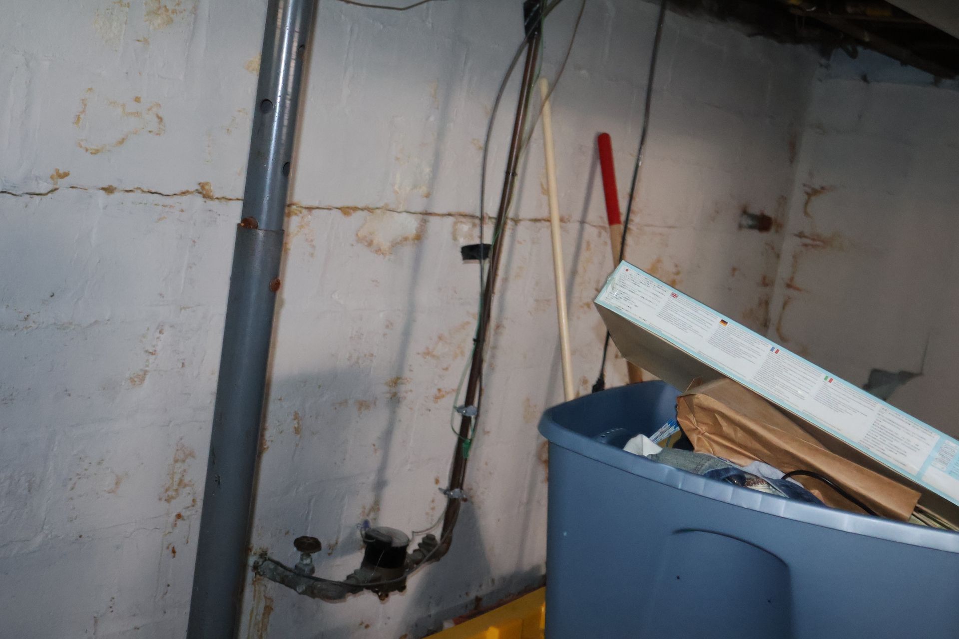 A basement corner shows a horizontal wall crack behind a gray support column, some loose wires, and storage bins.
