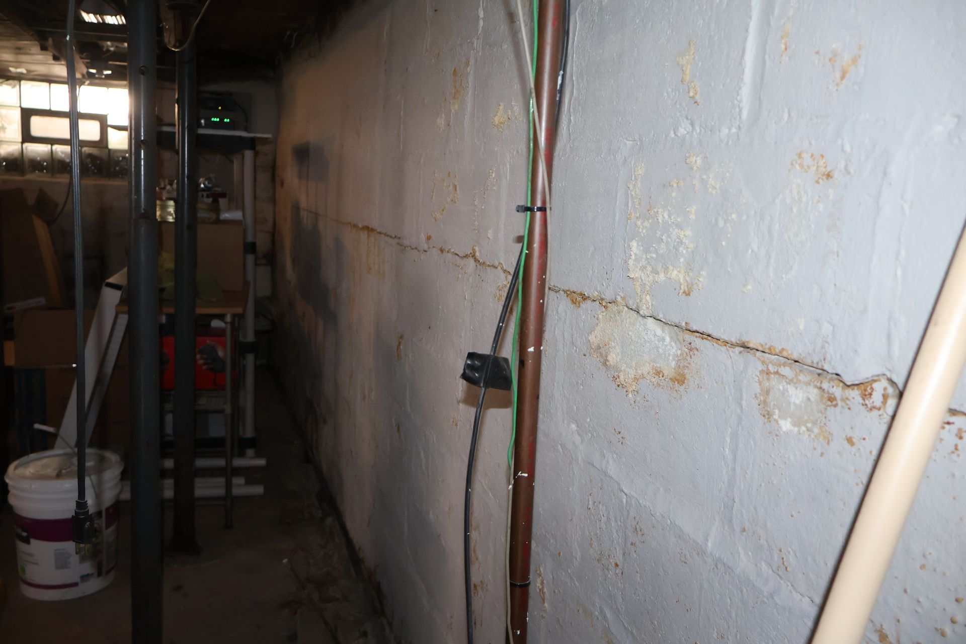 A horizontal crack runs along a painted white concrete block basement wall, showing signs of moisture and wear.