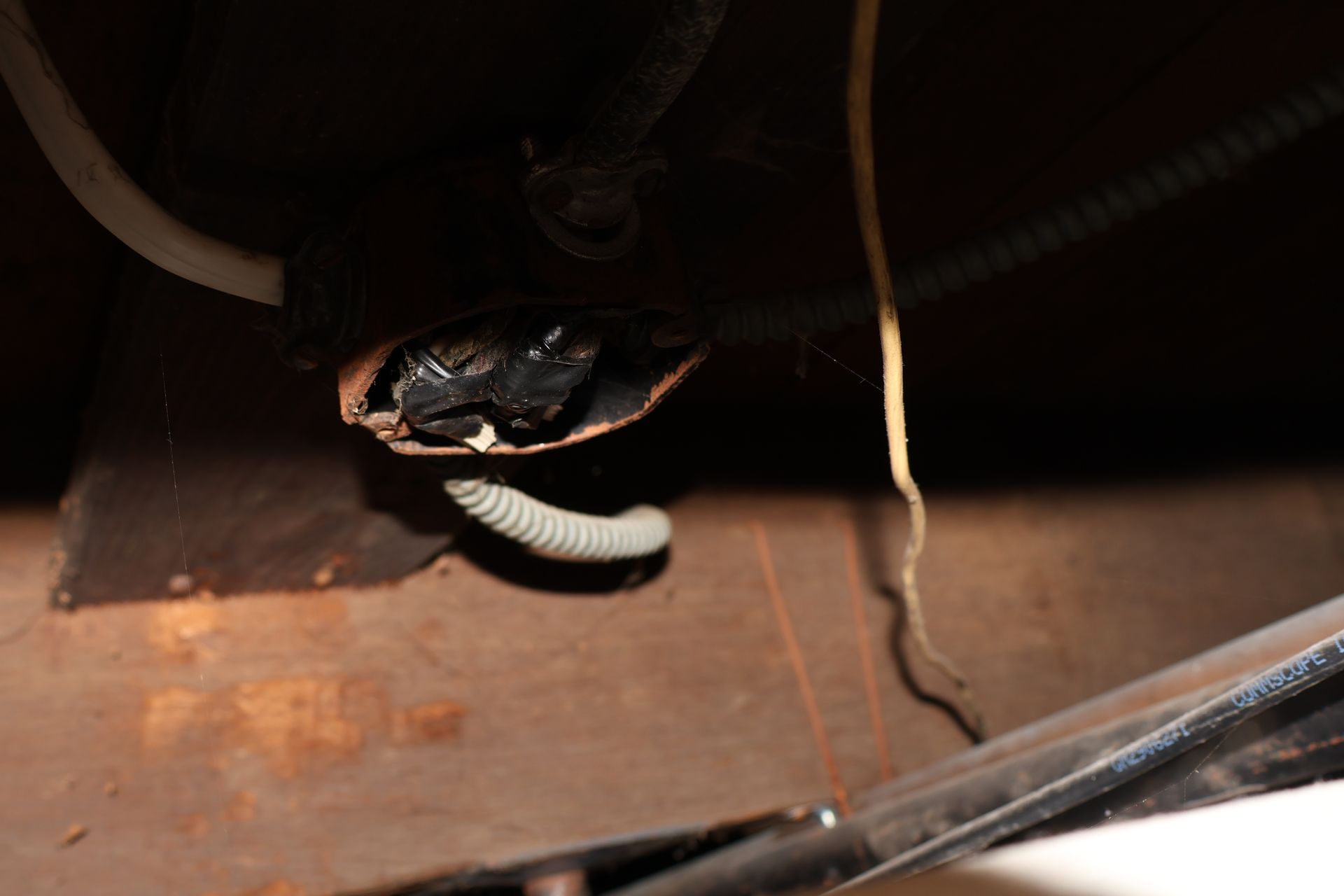 An exposed, rusted electrical junction box with visible wires in a dark, unfinished wooden area.