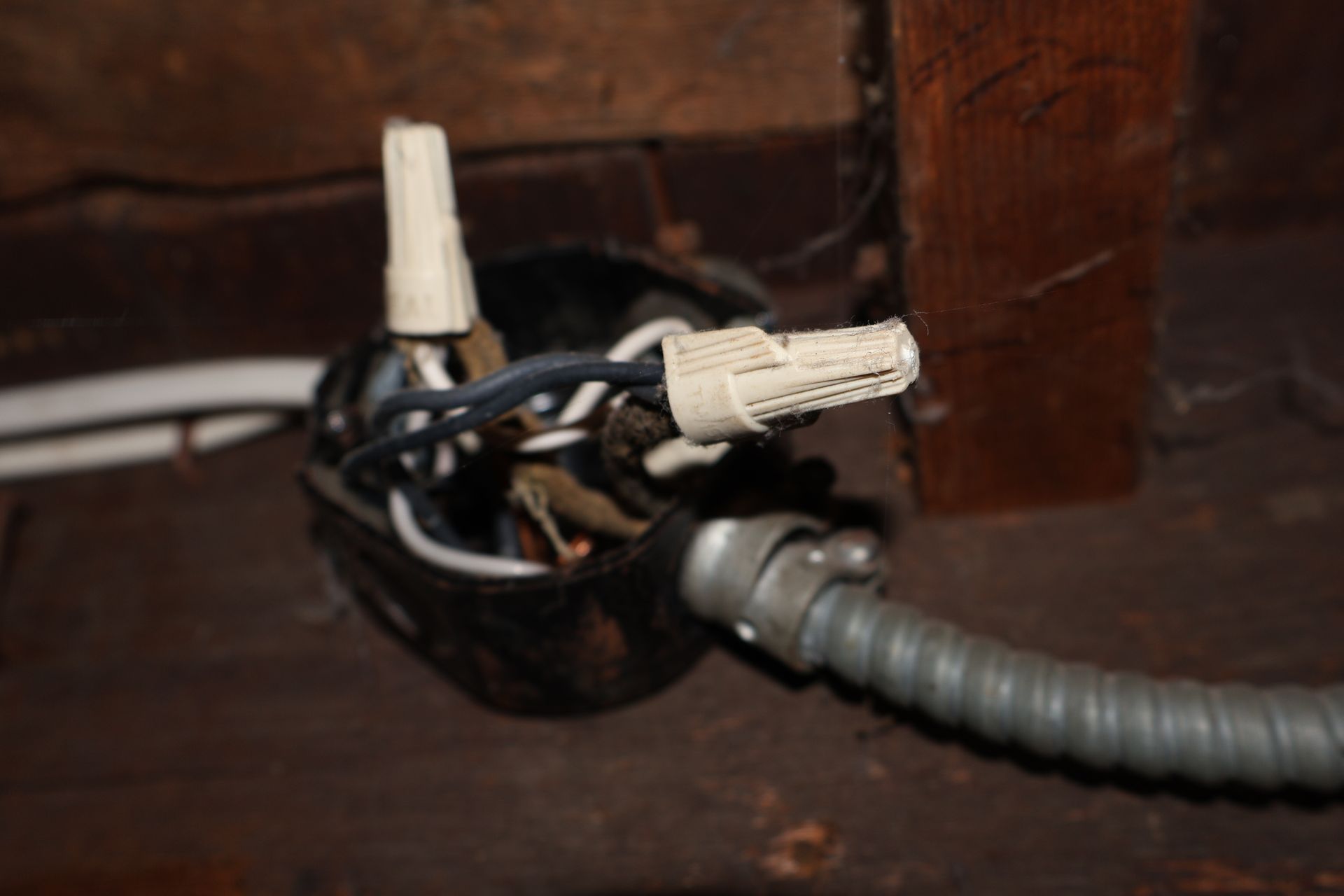 A metal electrical junction box with spliced wires secured by plastic wire nuts, attached to a flexible conduit.