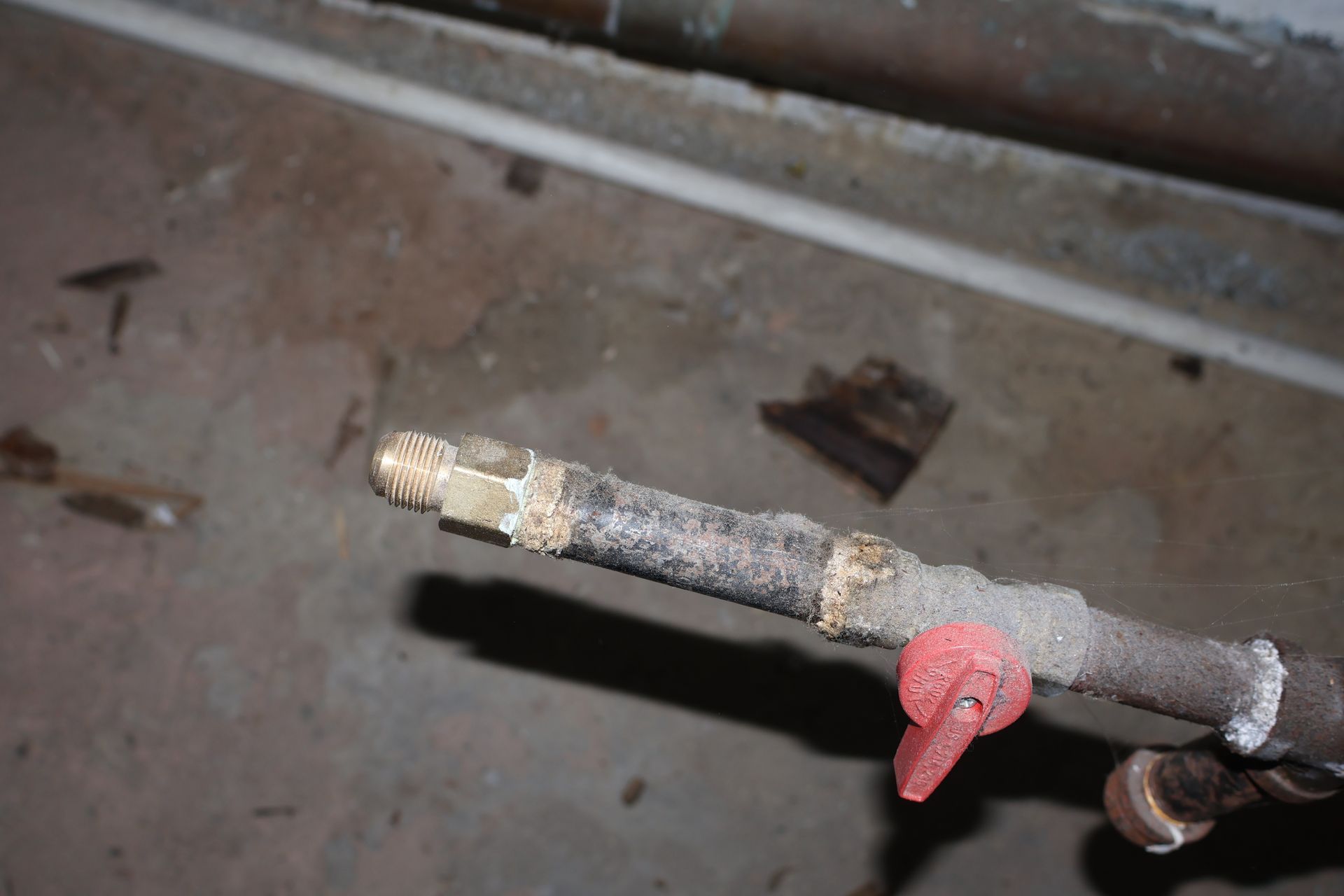 A close-up view of a metal pipe with a red shut-off valve, showing signs of corrosion and sediment buildup.
