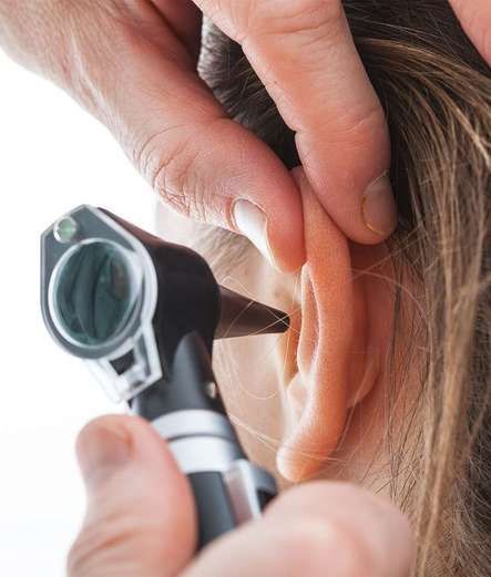 Person's ear being examined with an otoscope by a hand.