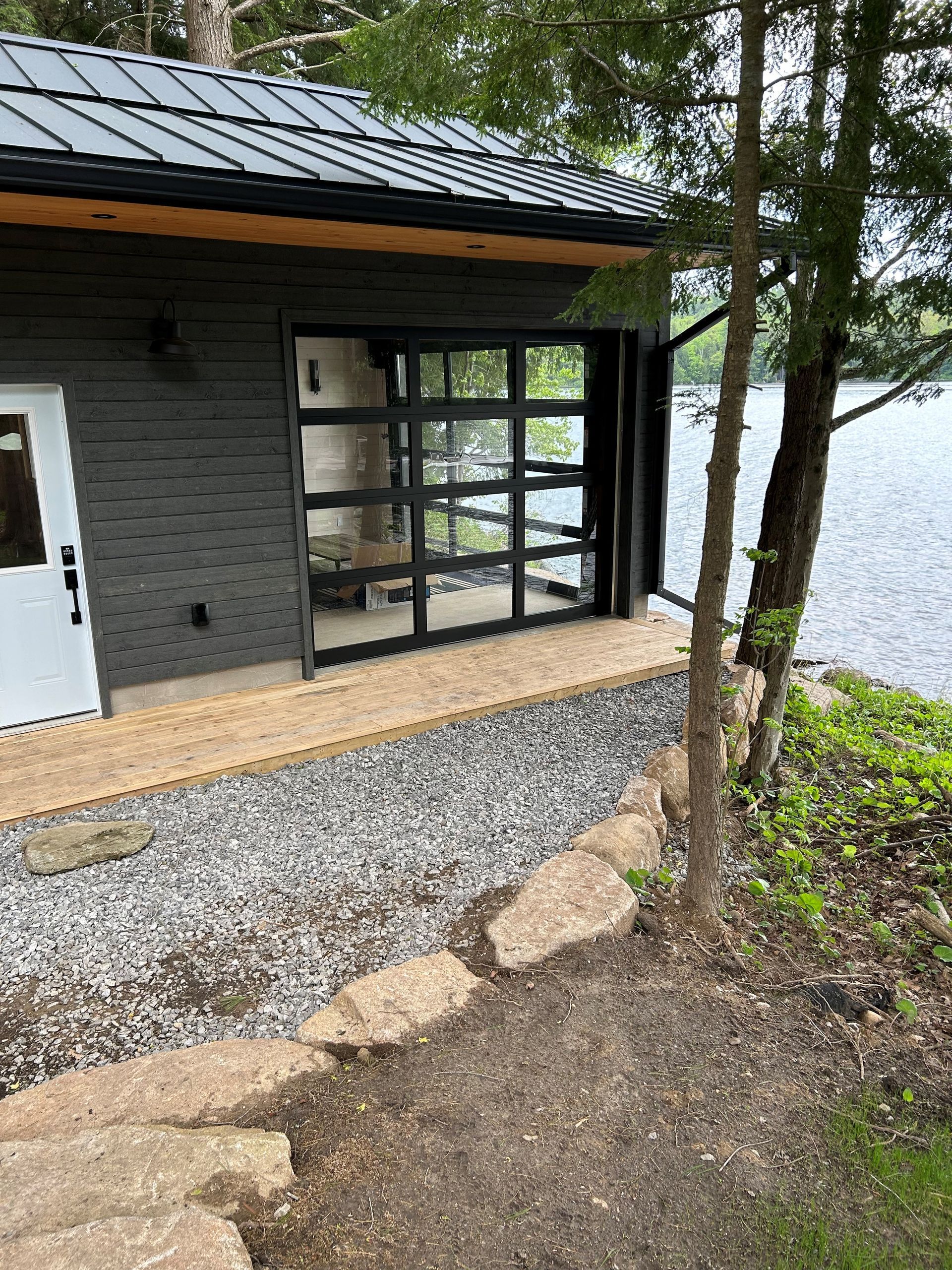 A small house with a large garage door next to a lake.