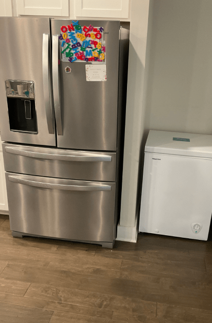 Stainless steel refrigerator with freezer, next to a white chest freezer in a kitchen.