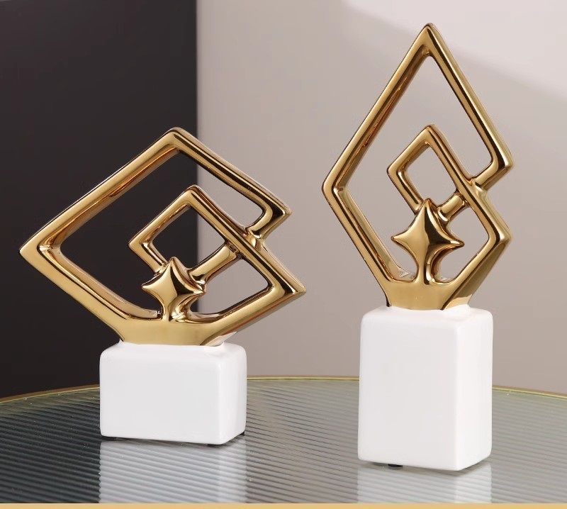Two gold geometric trophies on white bases against a dark background