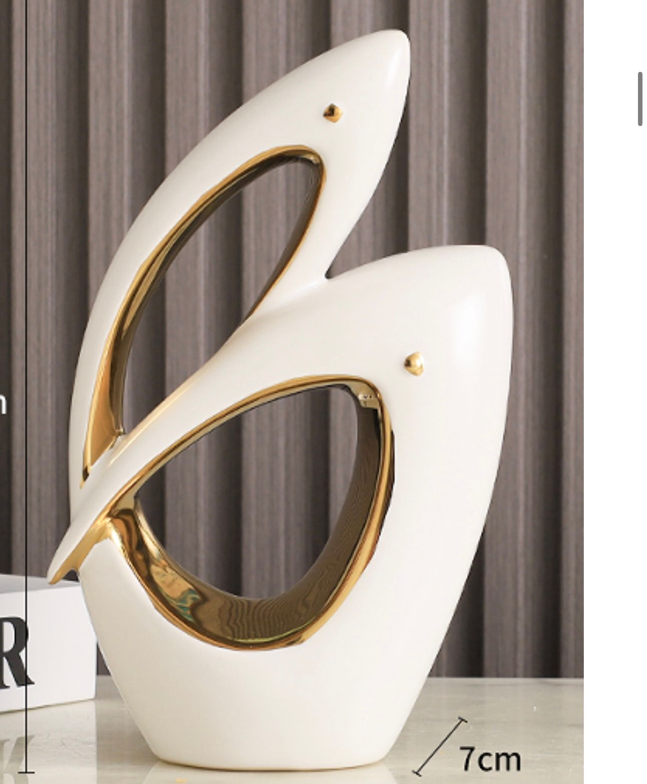 Abstract white and gold ceramic sculpture on a table, with curved cutout shapes