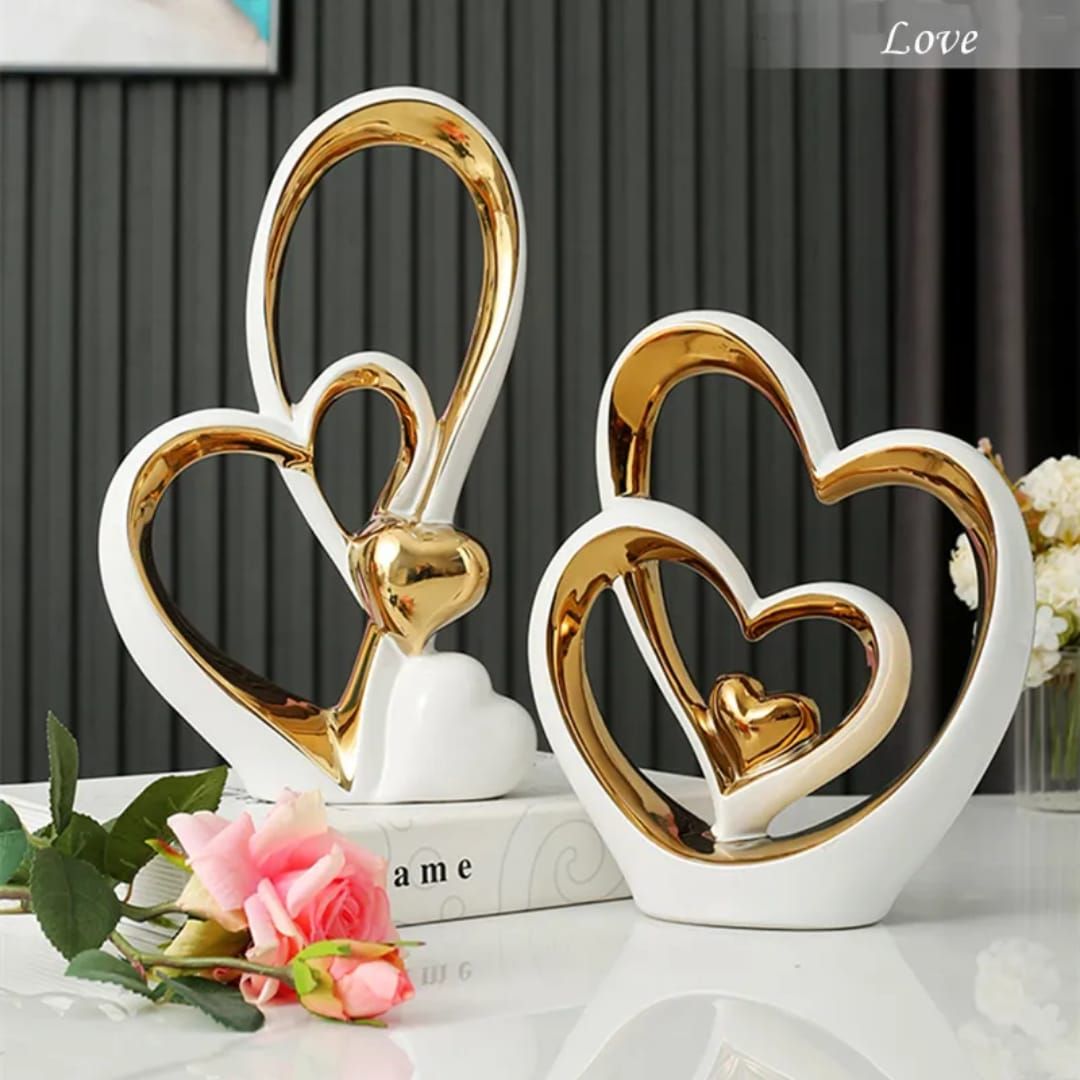 Decorative gold and white heart sculptures with pink rose on a white table