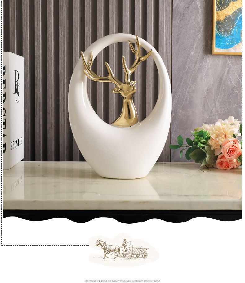 White oval tabletop sculpture with a gold deer inside, on a table with flowers and gray curtains.