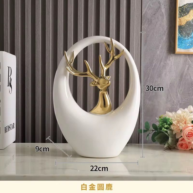 White oval tabletop sculpture with a gold deer inside, on a table with flowers and gray curtains.